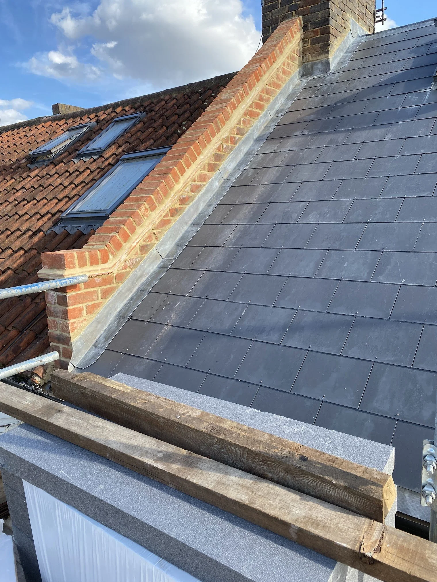 Roof with both traditional clay tiles and modern slate tiles, showing new roof installation or repair work with wooden and metal materials in the foreground.