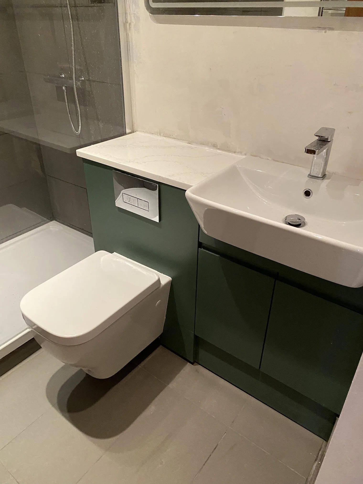 Bathroom with a white toilet, green vanity with a white marble countertop, a white sink with a chrome faucet, and a shower with a glass door and handheld showerhead.