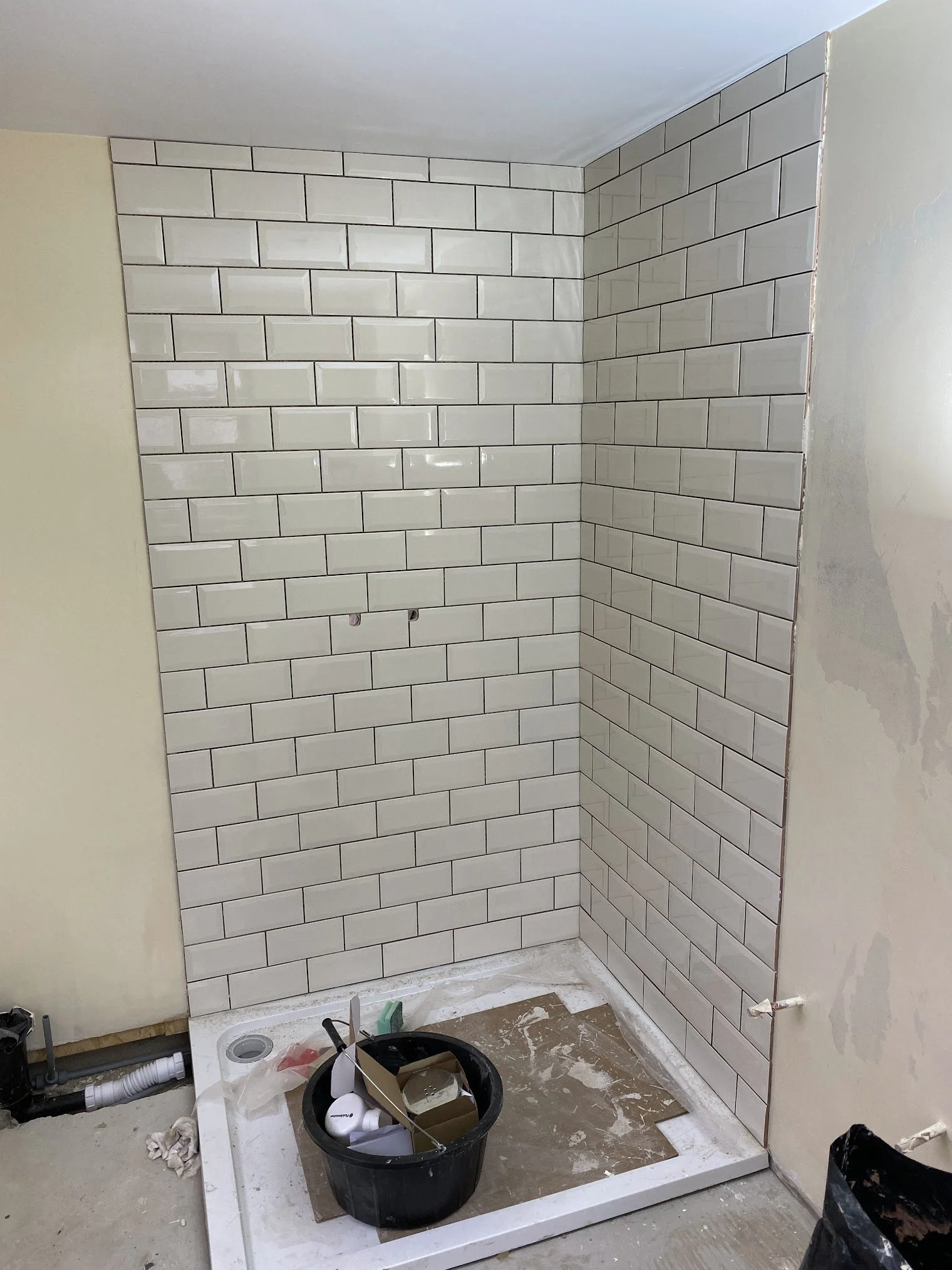 Bathroom under renovation with partially tiled wall, construction materials, tools, and plumbing fixtures on the floor.