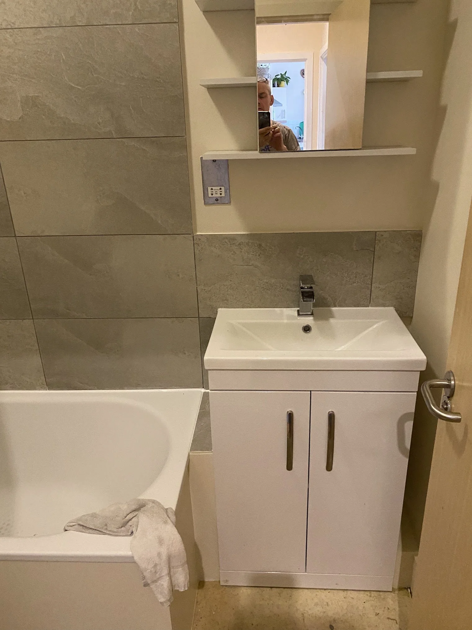 A bathroom with a small white sink, mirror, and cabinet, a towel on the sink, and a towel ring on the wall.