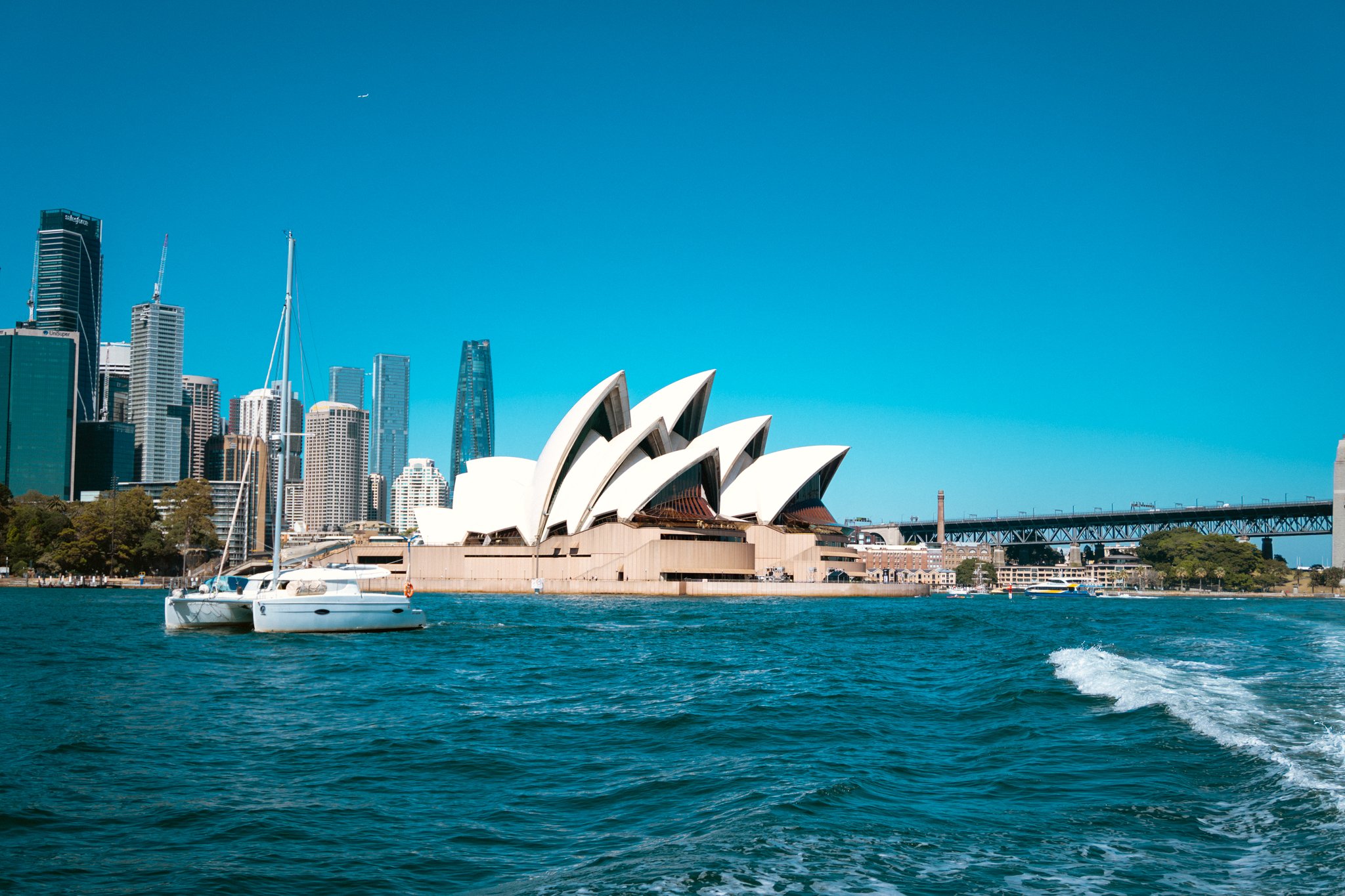 Sydney Opera House with city skyline and boats on the harbor under a clear blue sky.
