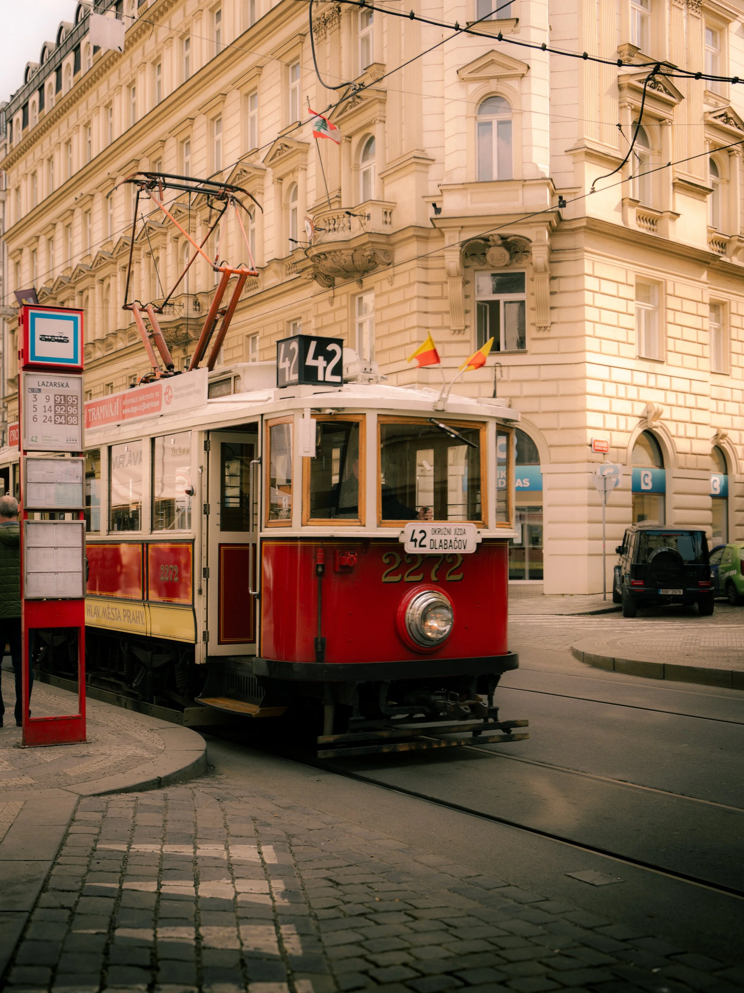 A red tram with the number 42 on a city street, on tracks, in front of a large cream-colored historic building with many windows.