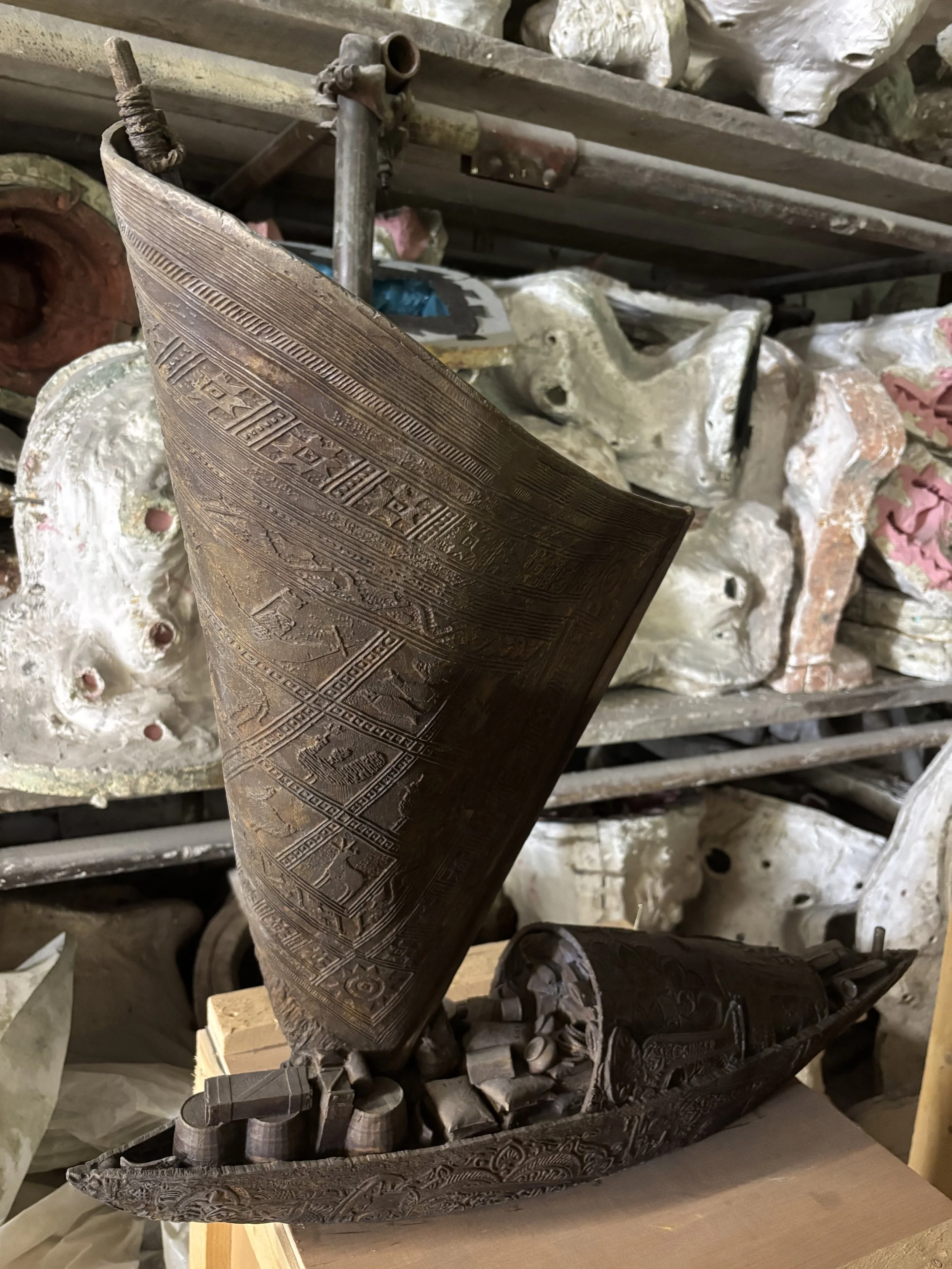 Hew Locke bronze boat sculpture from Cargoes at Arch Bronze, with decorated sails, barrels and timber cargo.