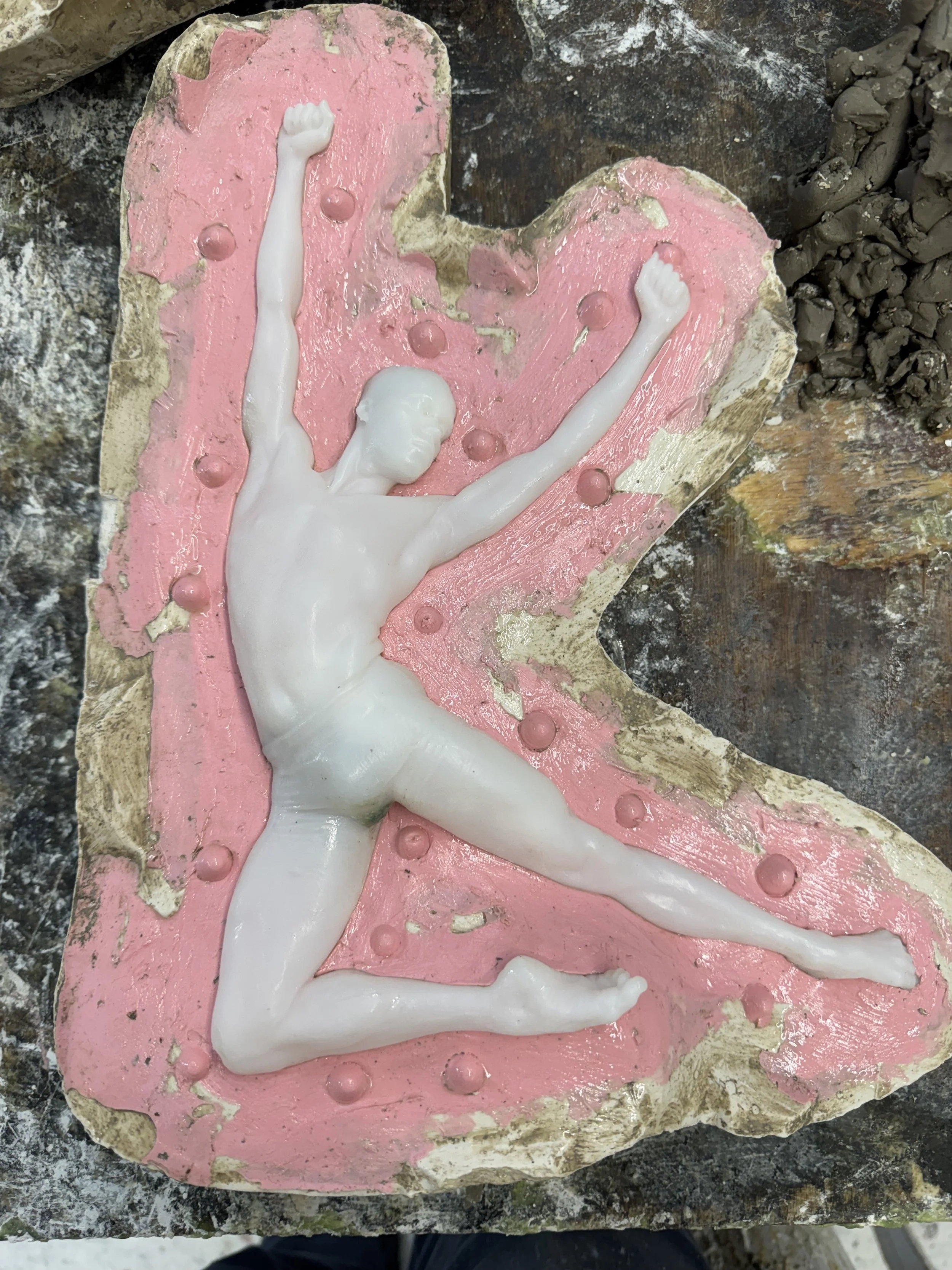 A sculpture of a dancing man with arms raised, embedded in a silicone and plaster mould.
