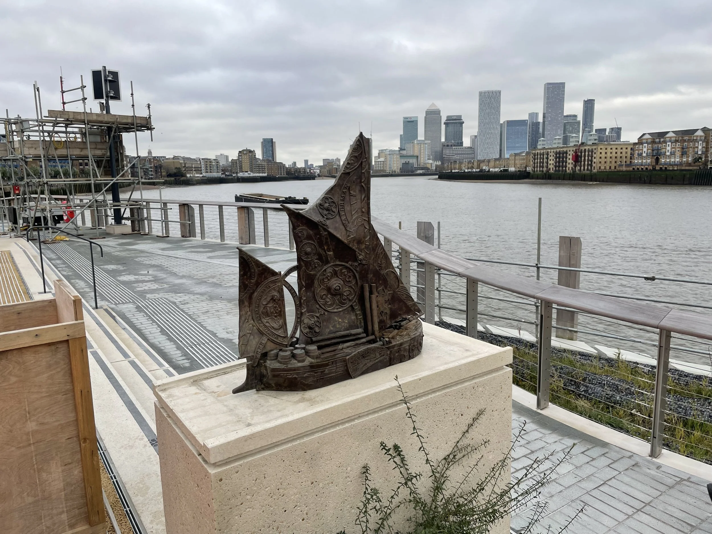 Hew Locke’s Cargoes bronze boat installed beside the Thames at King Edward Memorial Park, with Canary Wharf beyond.