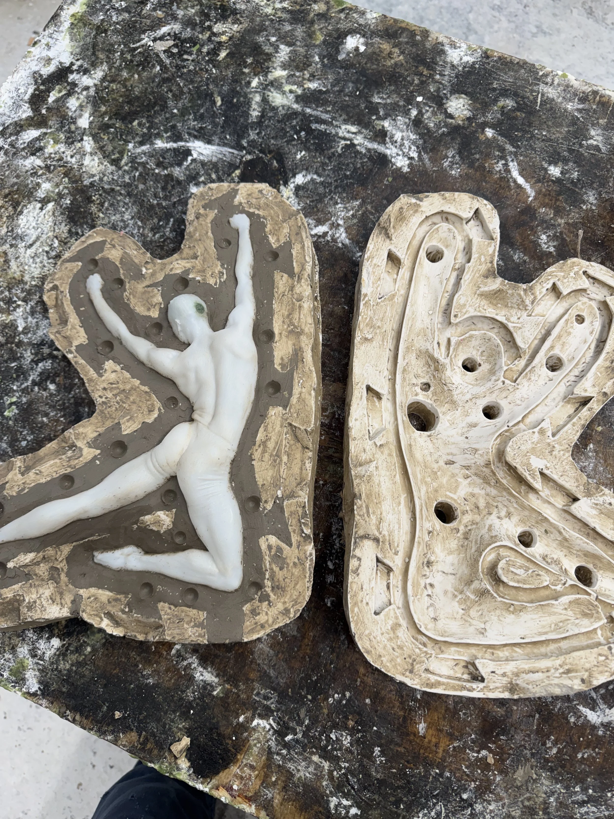 Two carved plaster molds of a dancing human figure on a weathered, paint-splattered wooden work surface.