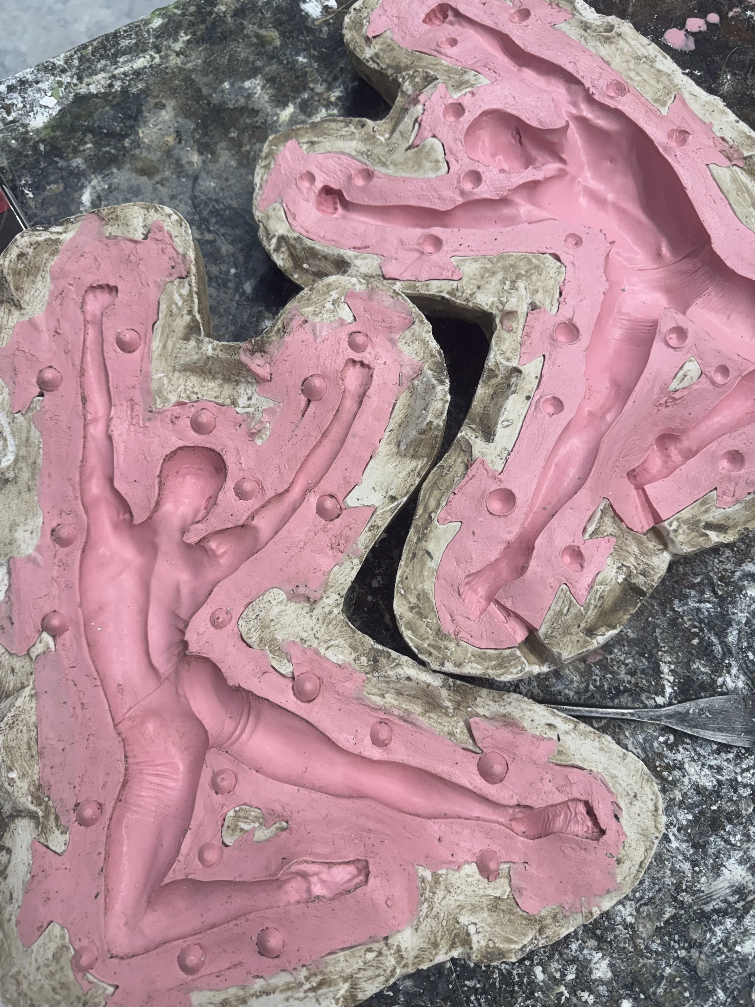 Close-up of a plaster mold with pink silicone rubber, revealing detailed impressions and textured surface, on a worktable.