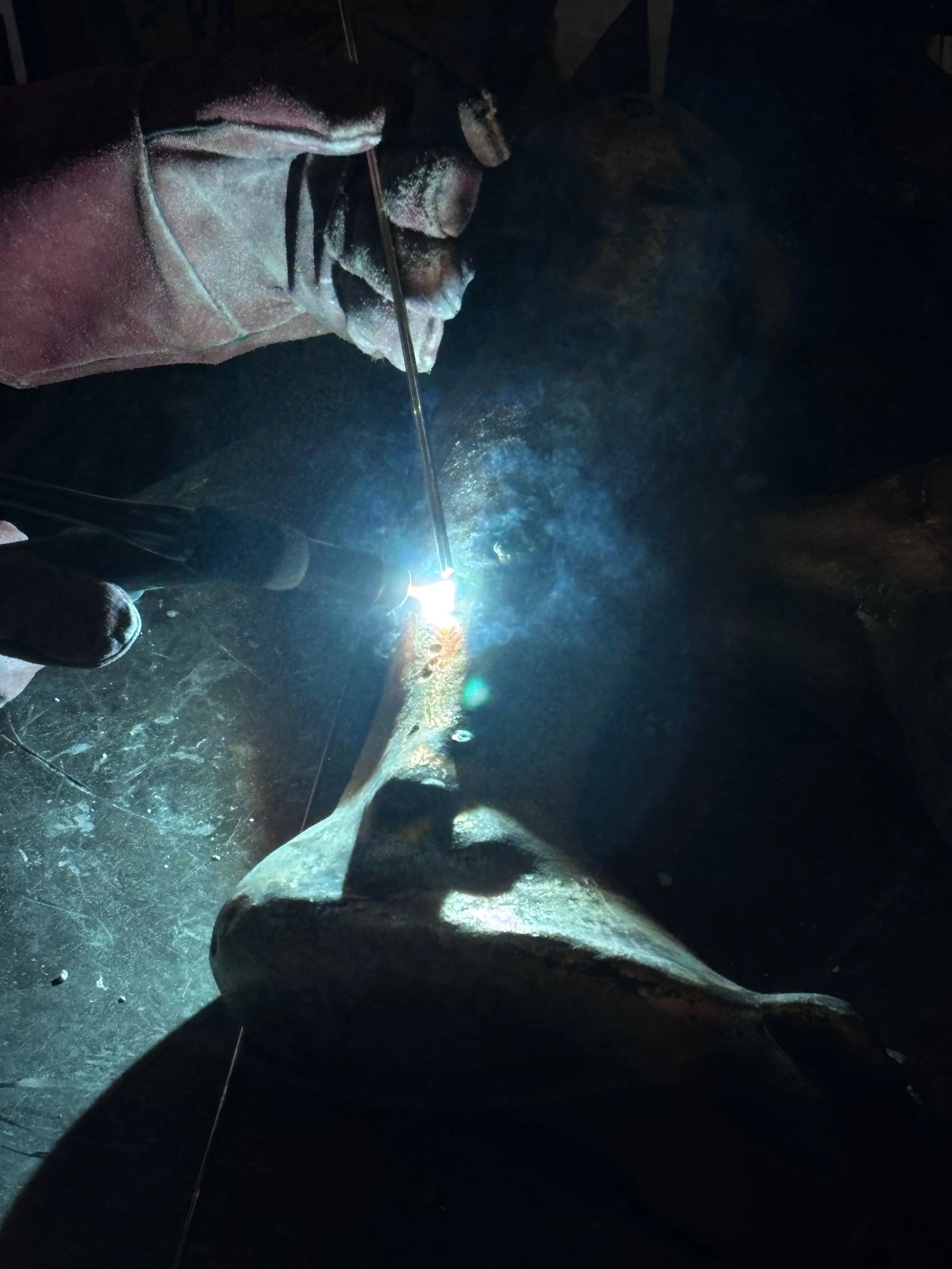 A person welding in a dark environment, wearing protective gloves and glasses, creating bright sparks and light.