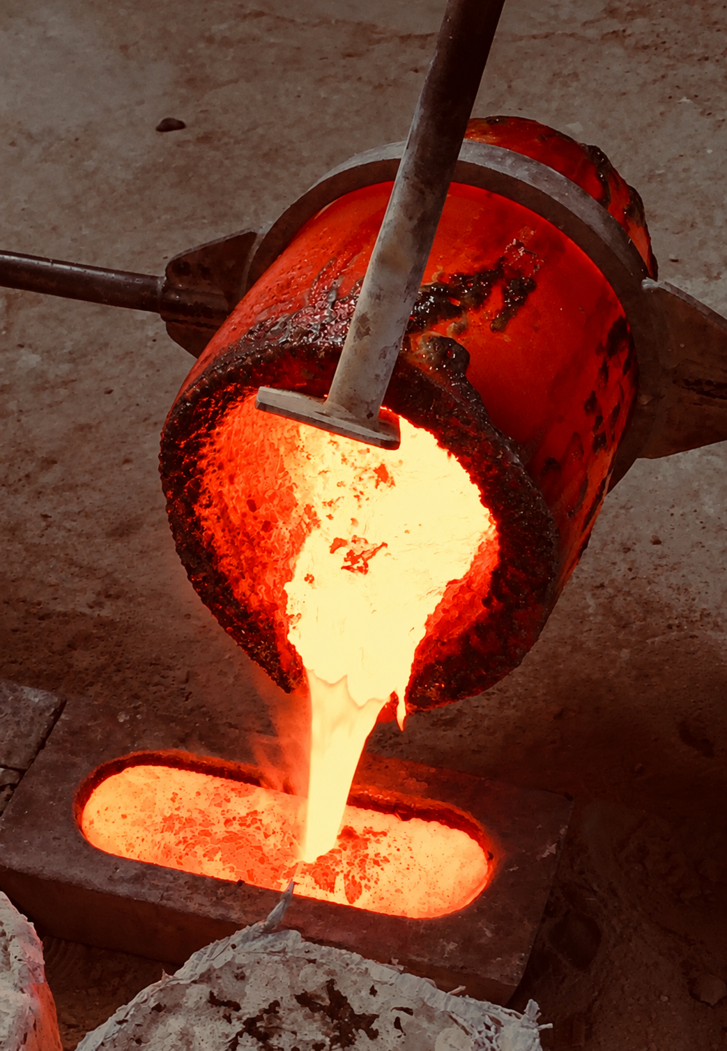 Molten metal being poured from a large container during a foundry process.
