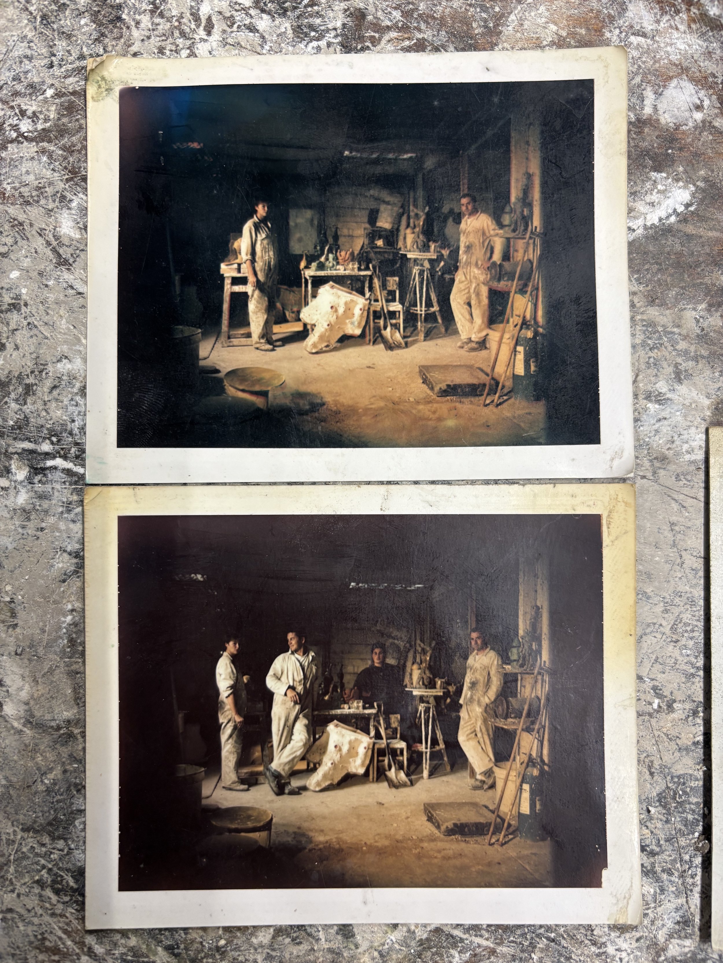 two Polaroid photographs of four people in a foundry workshop, standing around a workbench with tools and sketches, some wearing overalls, in a rustic, cluttered space with wooden walls and various tools and materials.