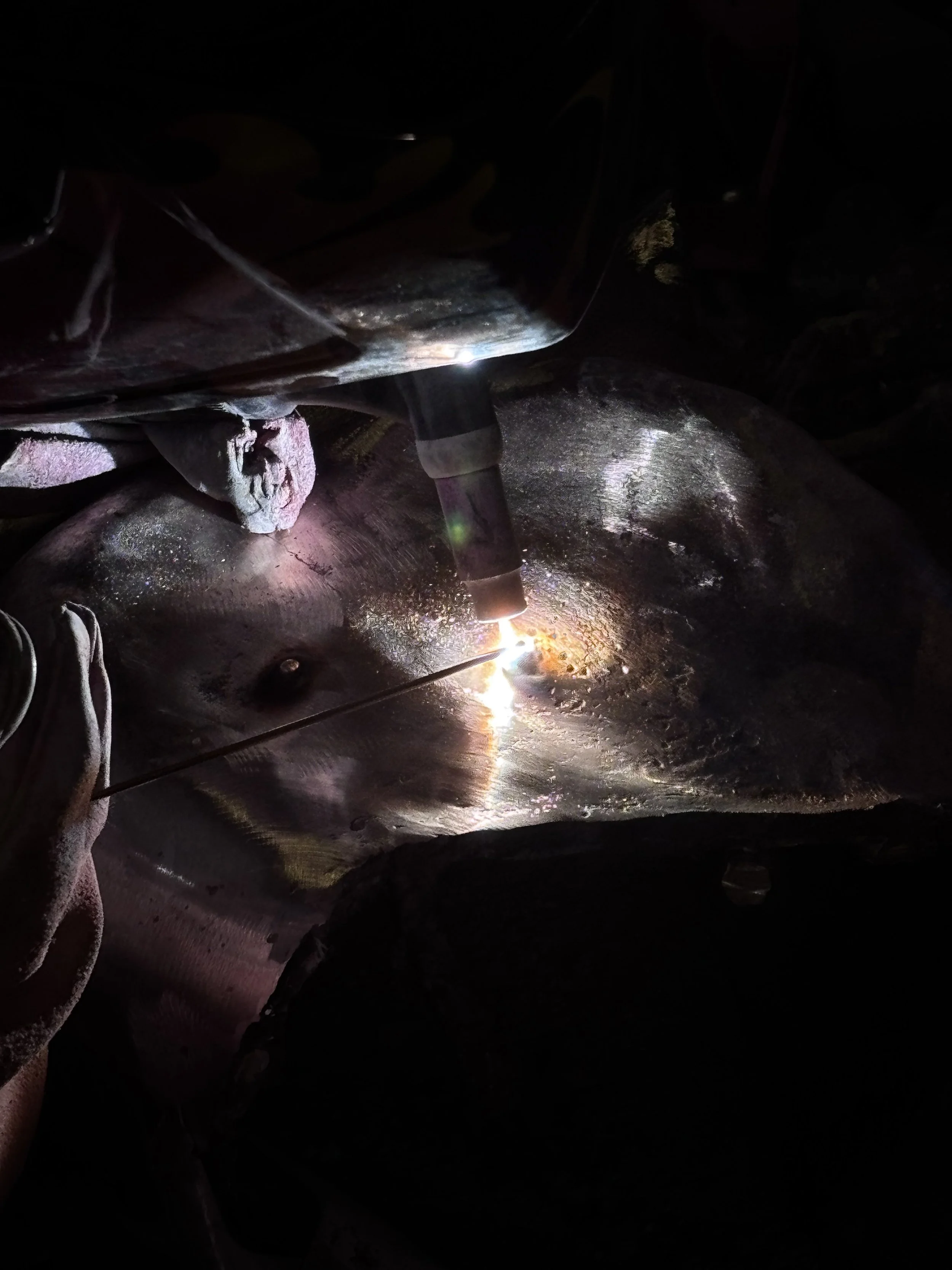 Close-up of a welding process on a metal surface, with sparks and bright light illuminating the dark background.