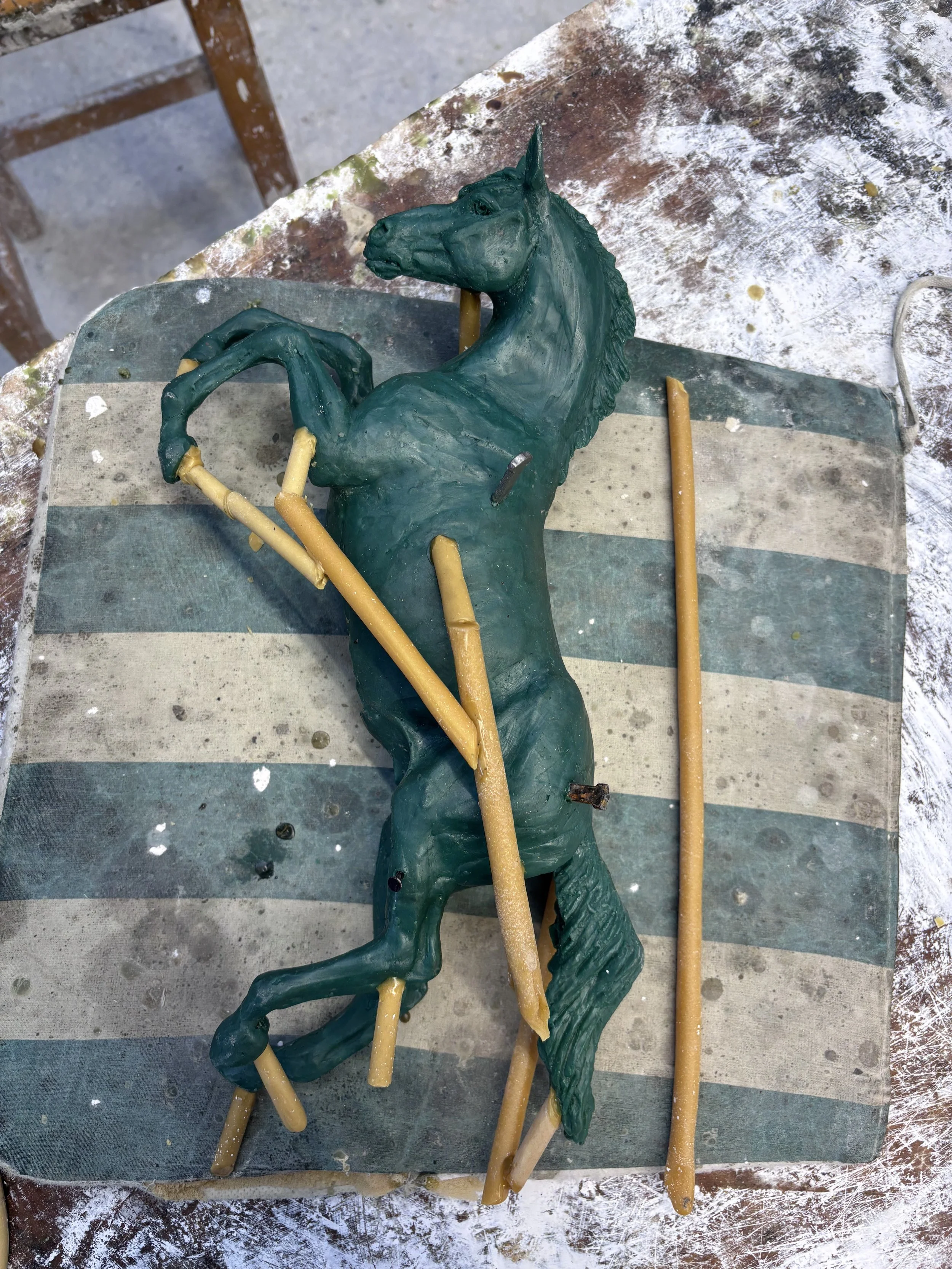 A green wax sculpture of a rearing horse on a worktable with various wax feeds.