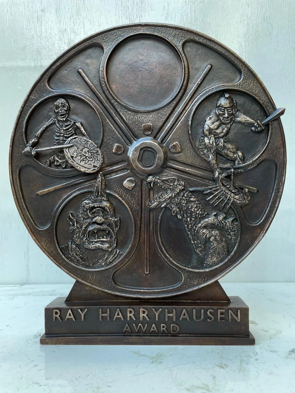 A bronze award trophy with six circular sections, each containing a detailed figure or face, and labeled at the base as 'Ray Harryhausen Award'.