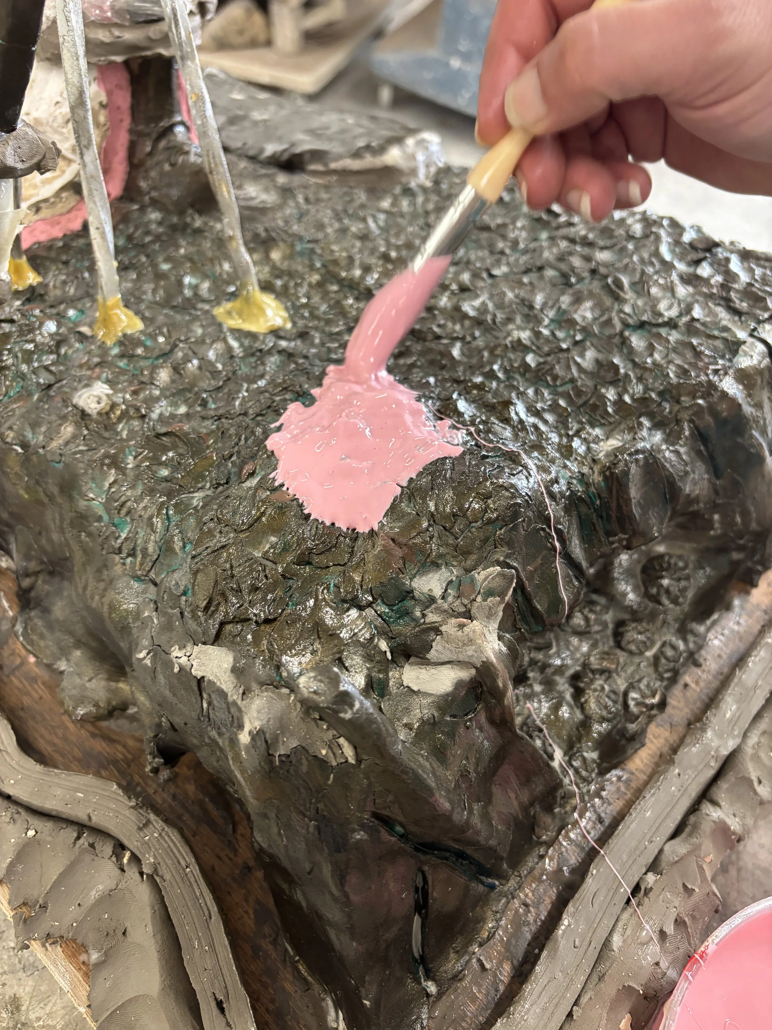 A person's hand applying silicone rubber to a sculpture with a small brush, in a sculpture or casting workshop.