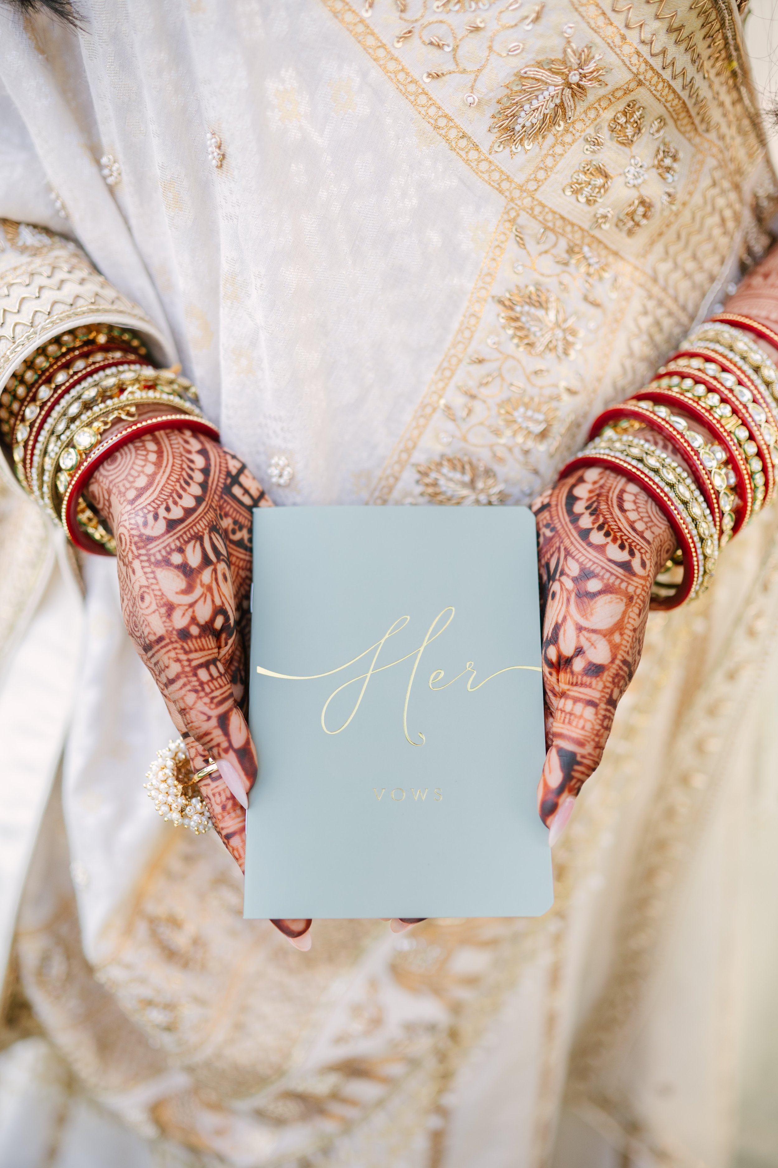 Bride holding vow book with henna and bangles
