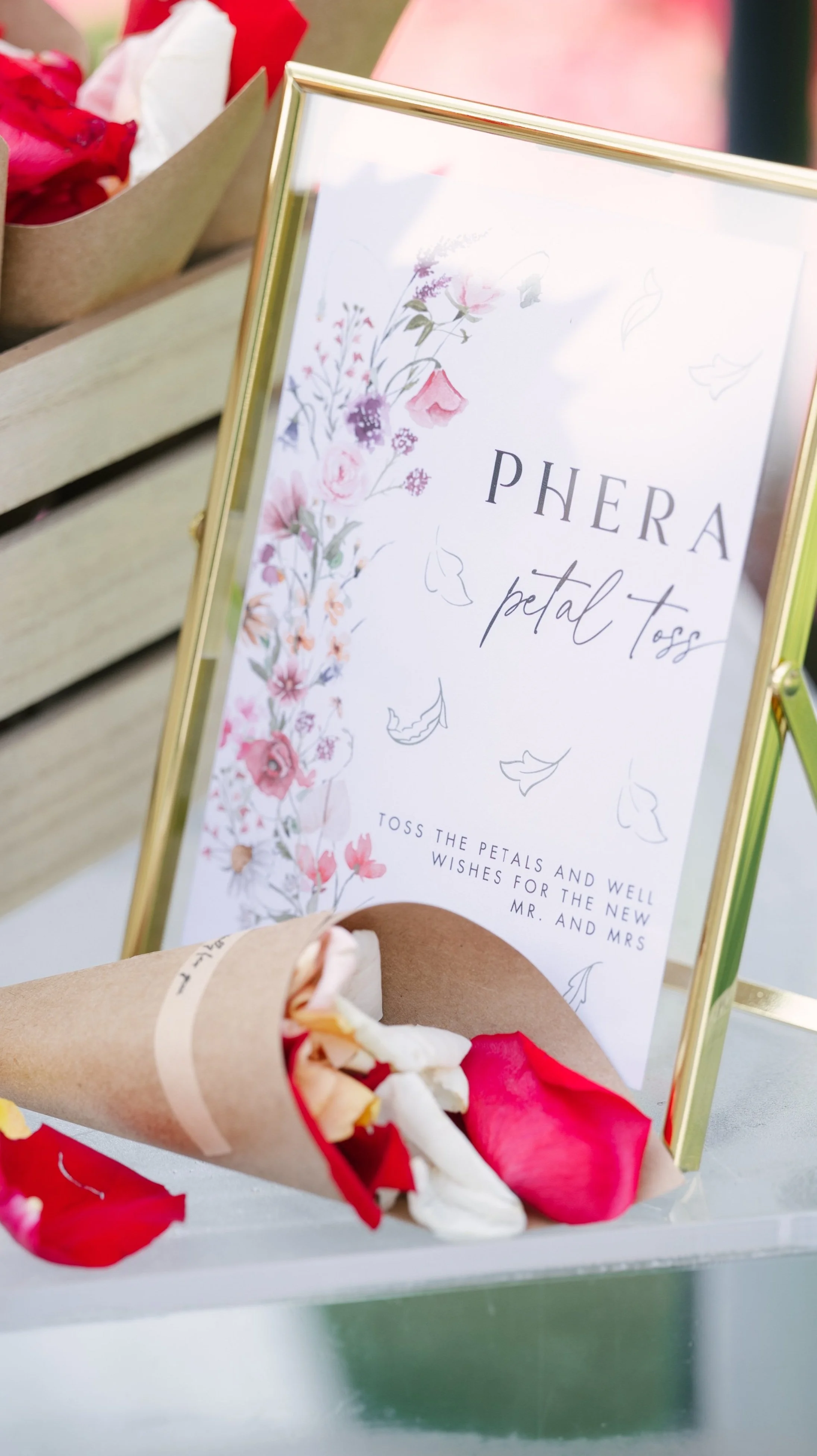 Wedding petal toss display with a sign reading 'PHERA petal toss', decorative floral design, and cones of red and white flower petals arranged for guests.
