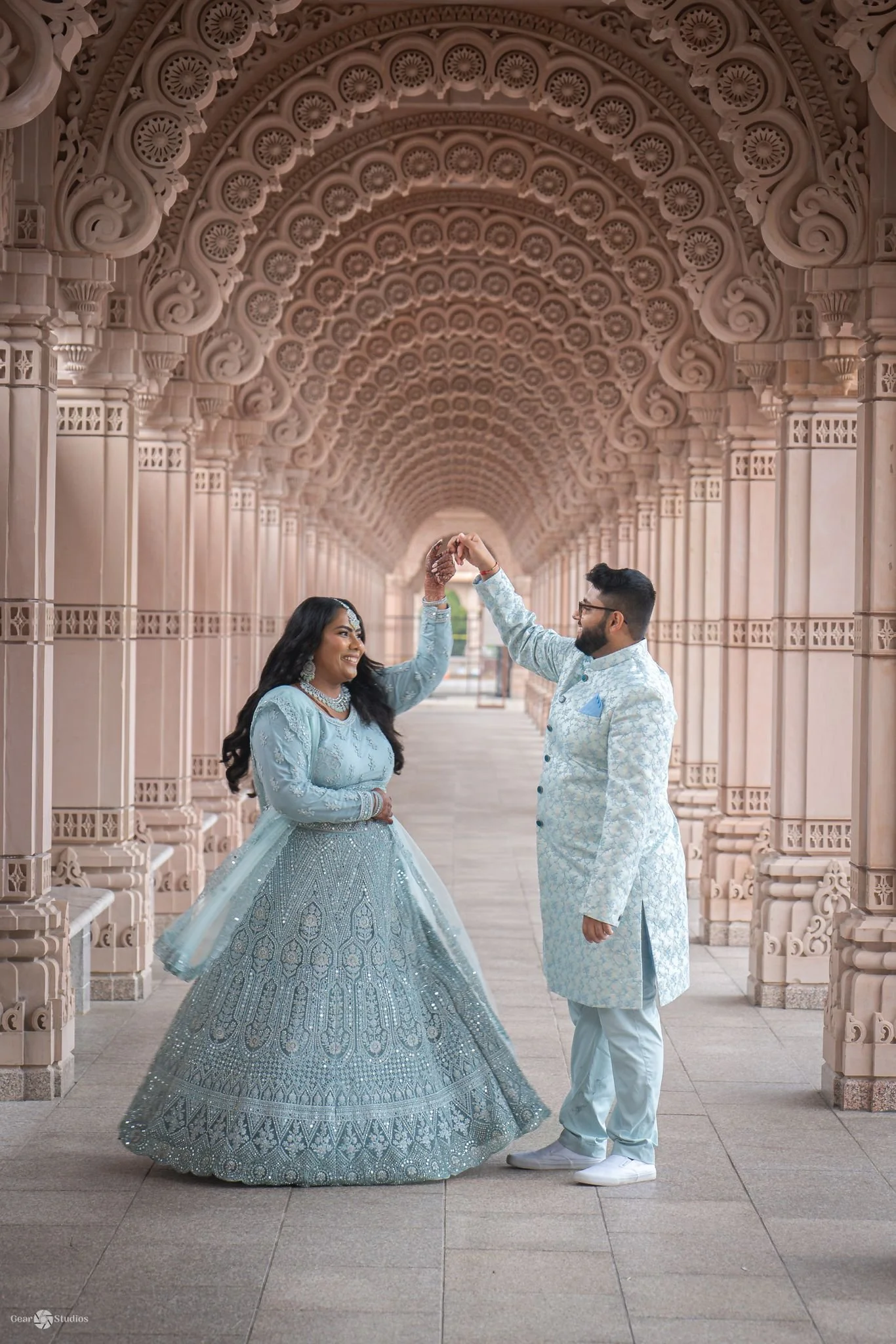 A couple in elegant, light blue traditional attire dancing under an ornately decorated archway.