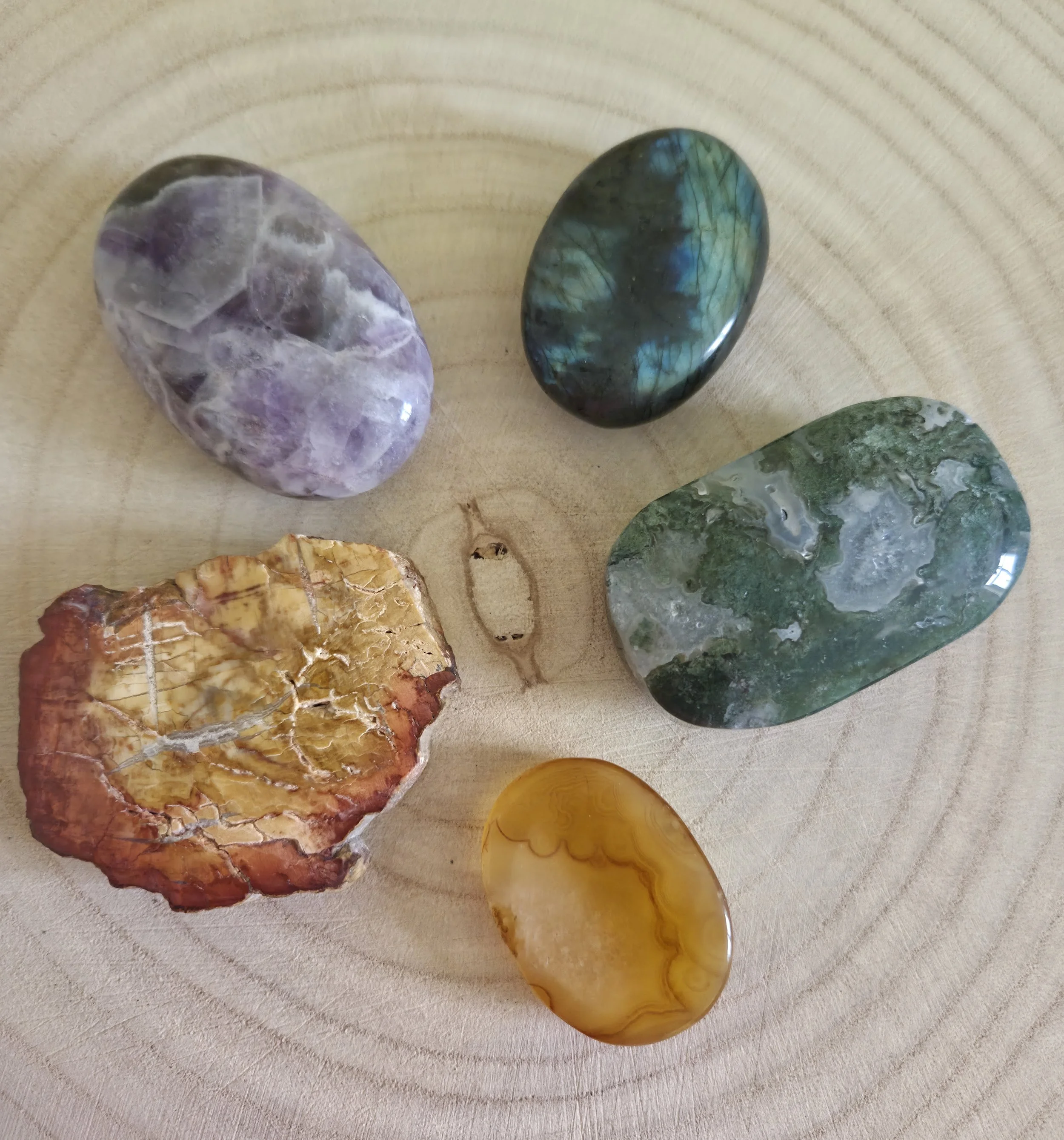 Various polished stones and minerals, including purple opal, iridescent labradorite, green malachite, and yellow calcite, arranged on a light-colored wooden surface.