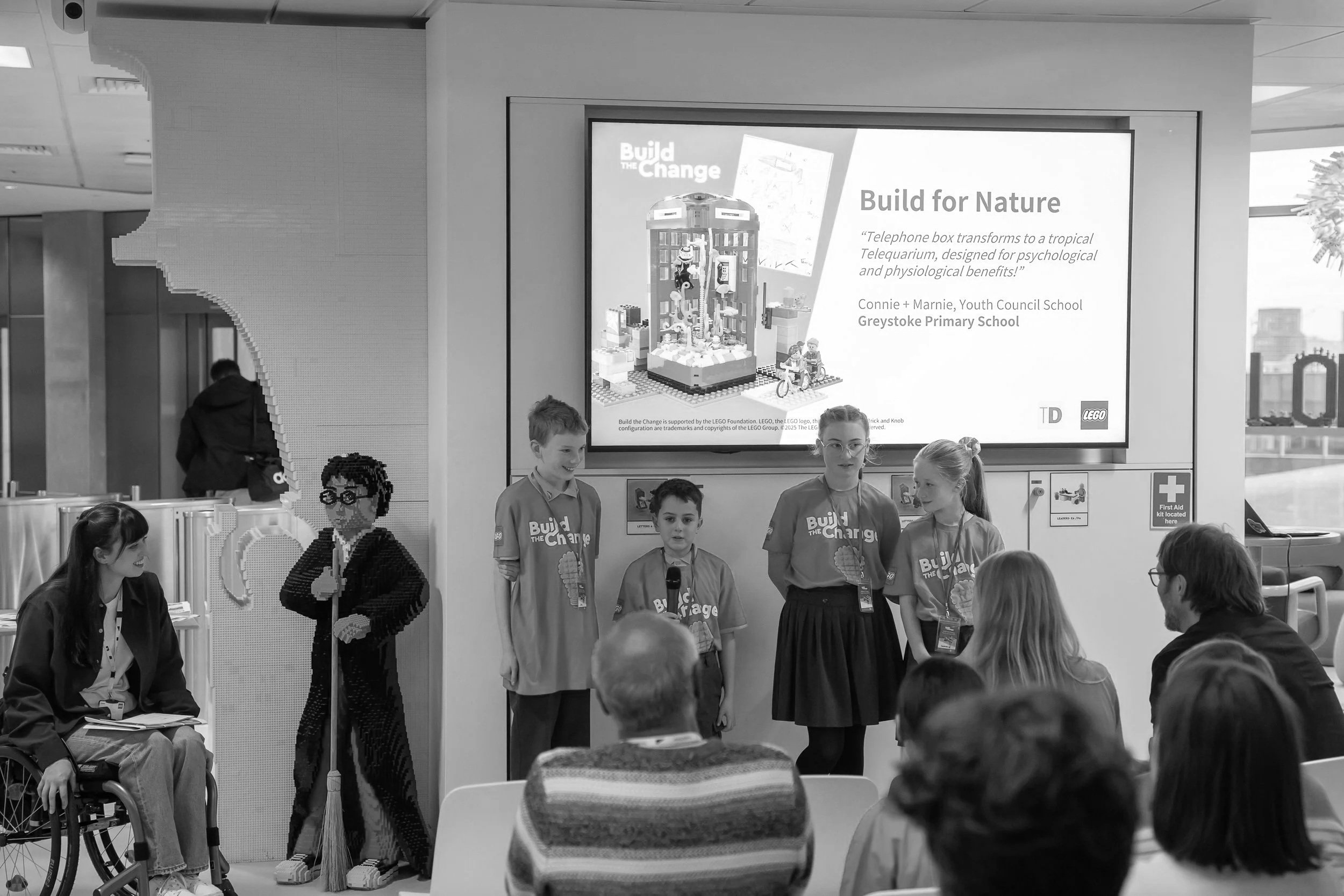 Photo of 4 primary students presenting their ideas to a room full of inclusive design experts as part of the LEGO Build the Change Youth Council Showcase event at LEGO HQ in London.