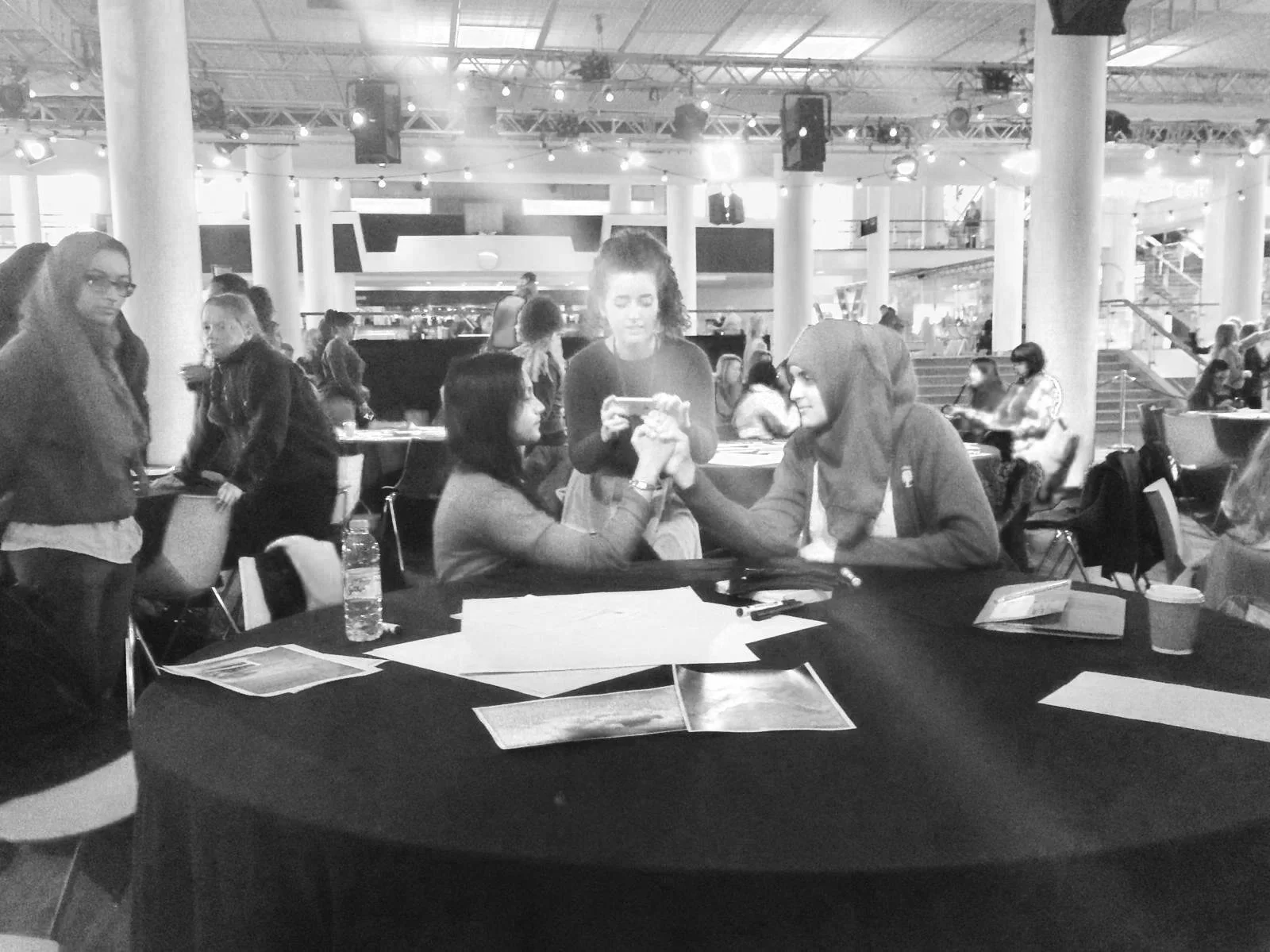 Black & white photo of two female students posing for a photo, having an arm wrestle, at the Women of the World Festival 2015 GirlHood takeover workshop.