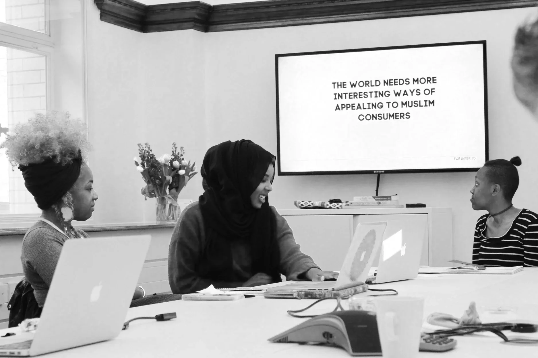 Black & white photo of 3 females working on a creative brief during The GirlHood Creative Traineeship at FCB Inferno. The screen reads: The world needs more interesting ways of appealing to Muslim consumers.