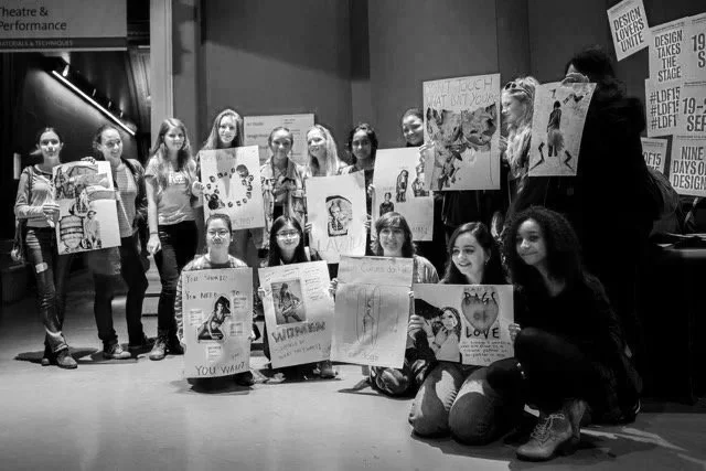 Black & white photo of a large group of girls posing with protest art they had made at the V&A during a GirlHood creative voice workshop.