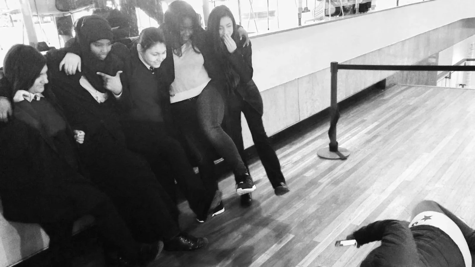 Black & white photo of a group of girls posing for a photo being shot by a girl lying on the floor. They're smiling and having fun. Taken at the WOW Women of the World Festival GirlHood launch in 2015.