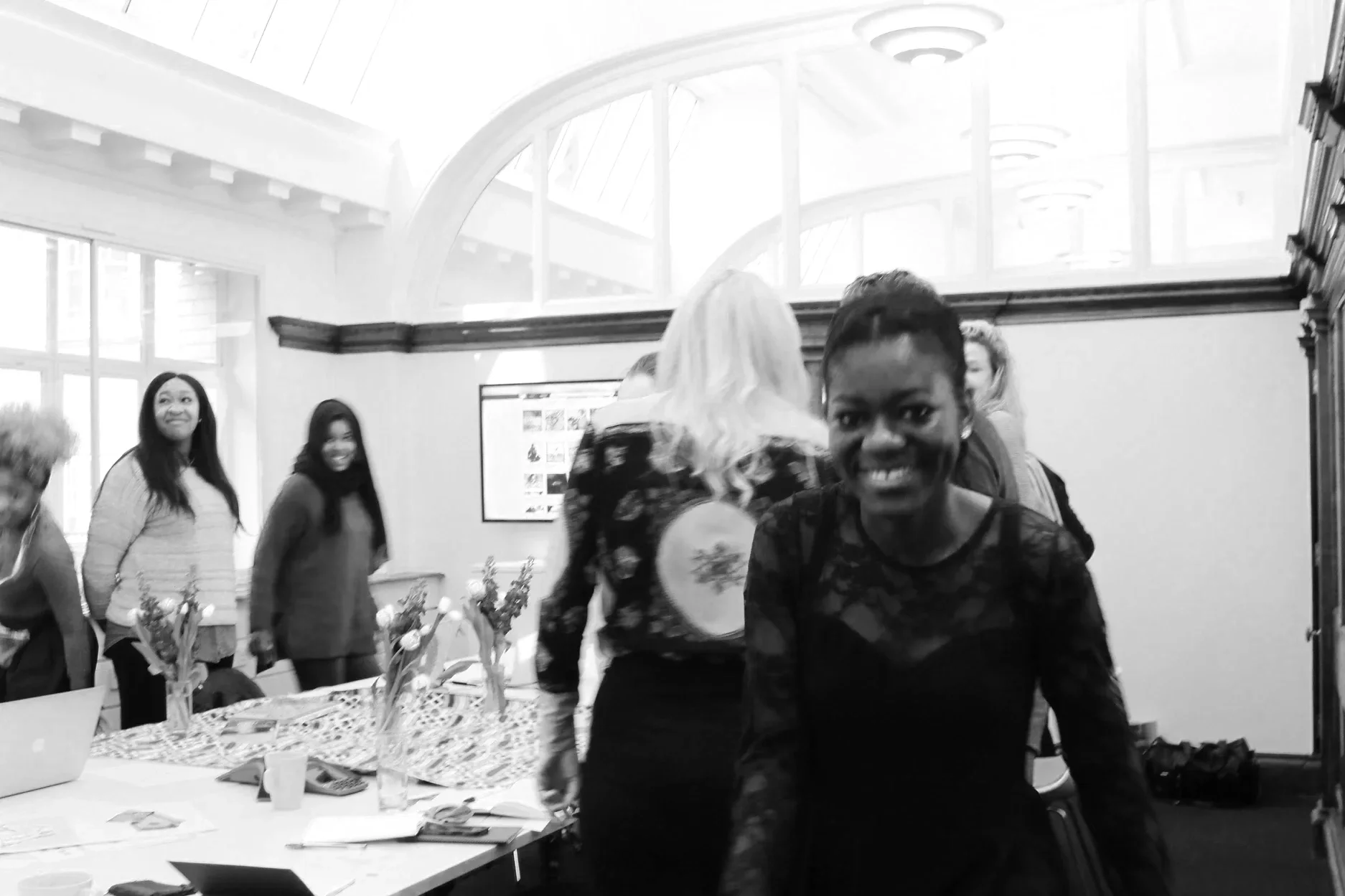 Black & white photo of participants of The GirlHood Creative Traineeship, in a boardroom at FCB Inferno. They are smiling and standing behind their chairs.