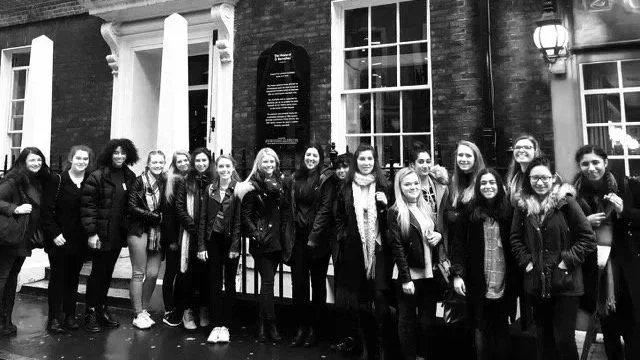 A large group of female students pose for a photo outside a building having just taken part in a GirlHood creative workshop designing advertising campaigns promoting a menstruation equality charity.