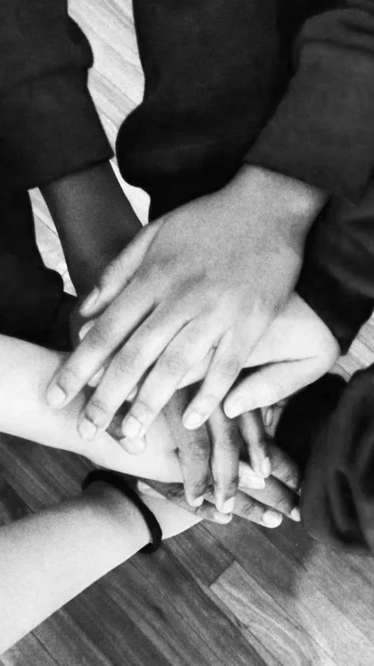 Black and white photo of students hands, stacked on top of each other, at a workshop.