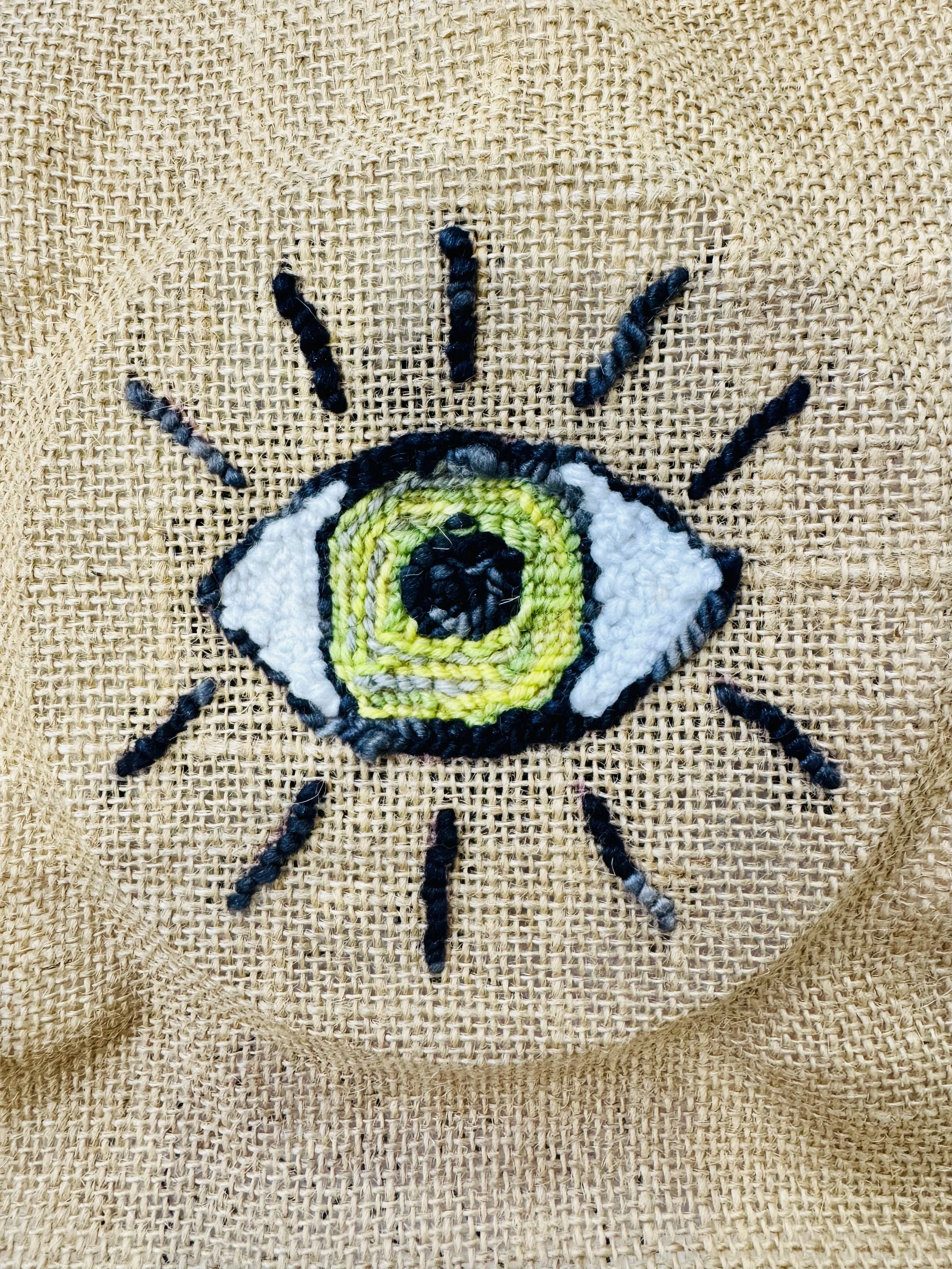 an image of a piece of Natalie's artwork - an eye on hessian fabric done with a punch needle and yarn