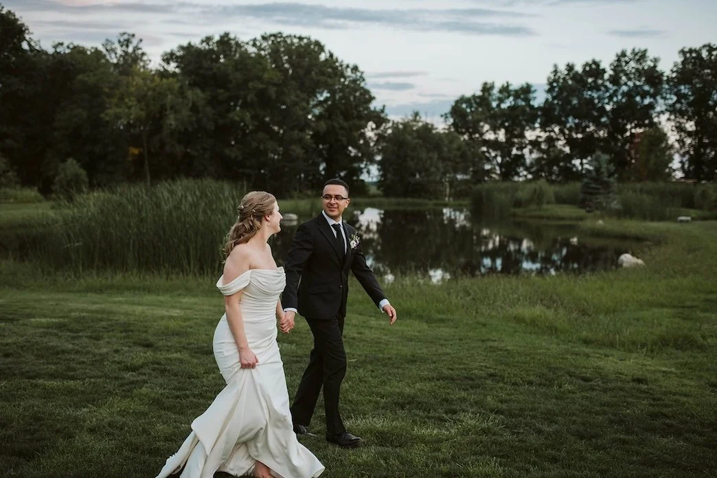 bride and groom walking next to pond at sunset
