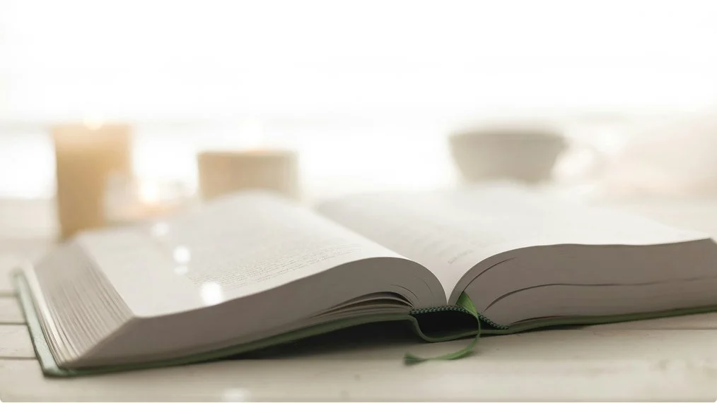 Open book on a table with blurred cups in the background.