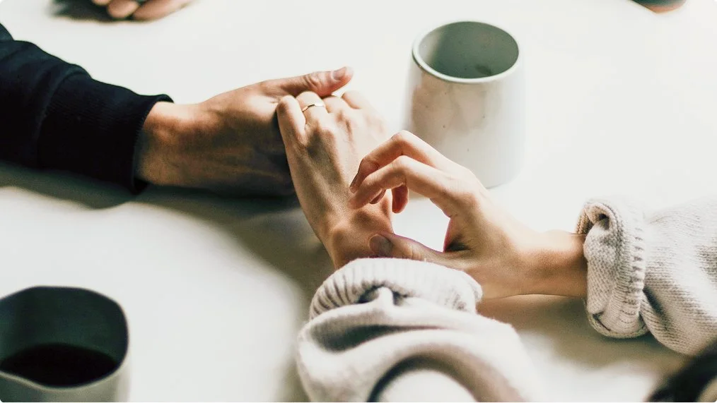 Two people holding hands on a table with coffee mugs.