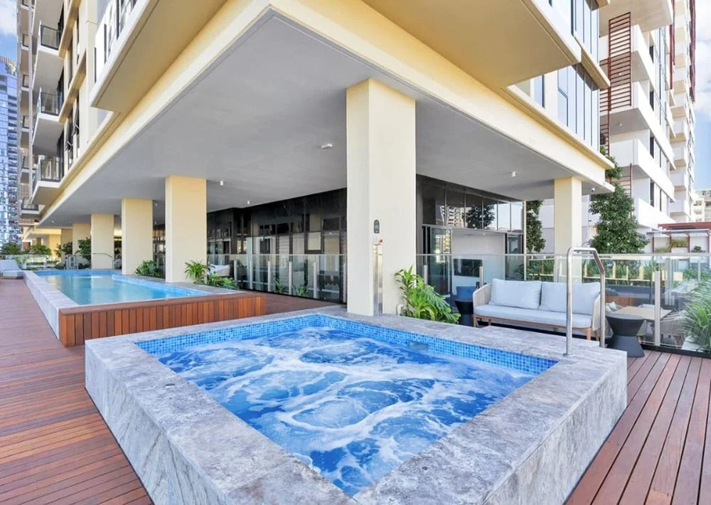 Outdoor spa and pool beside an apartment building, with timber decking and seating.