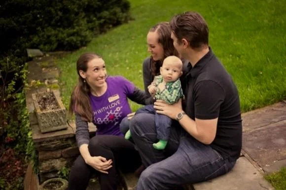 A family of three sitting on a stone ledge outdoors with a woman, a man, and a baby, smiling and interacting.