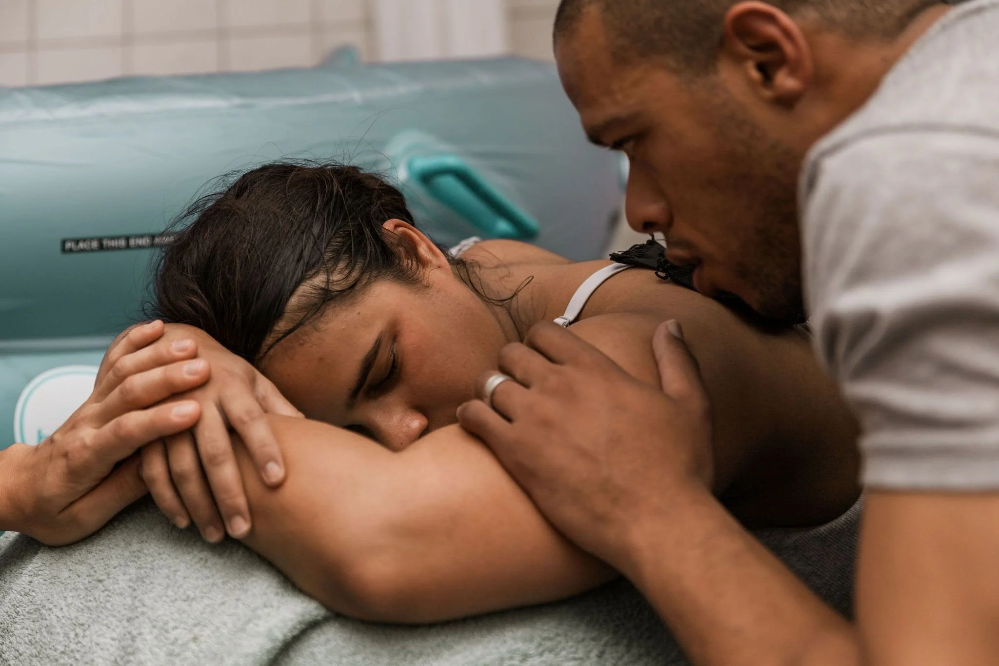 A man is giving a comforting hug to a woman lying on a medical bed, possibly in a hospital or healthcare setting.