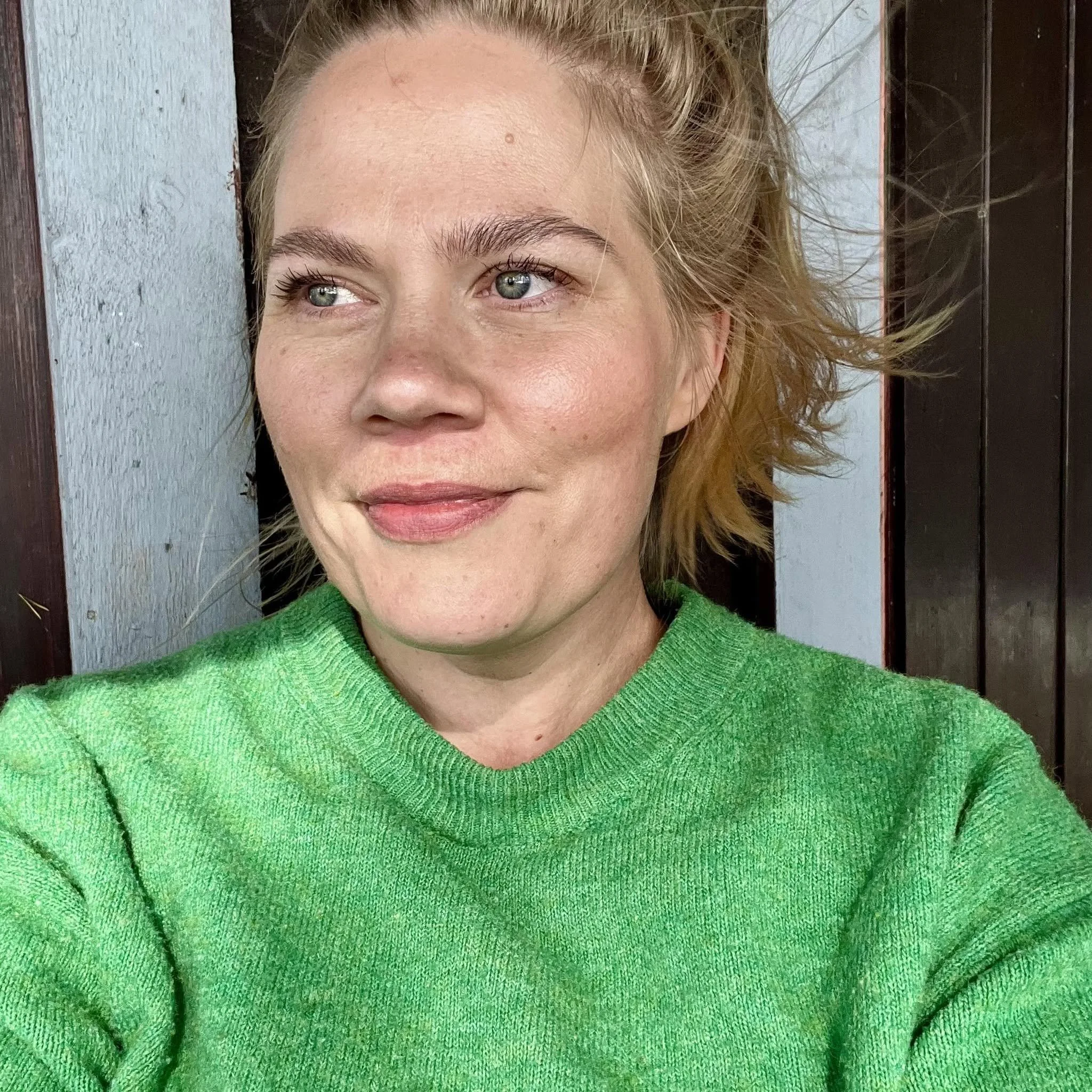 Close-up portrait of a smiling woman with blonde hair wearing a bright green sweater outdoors.