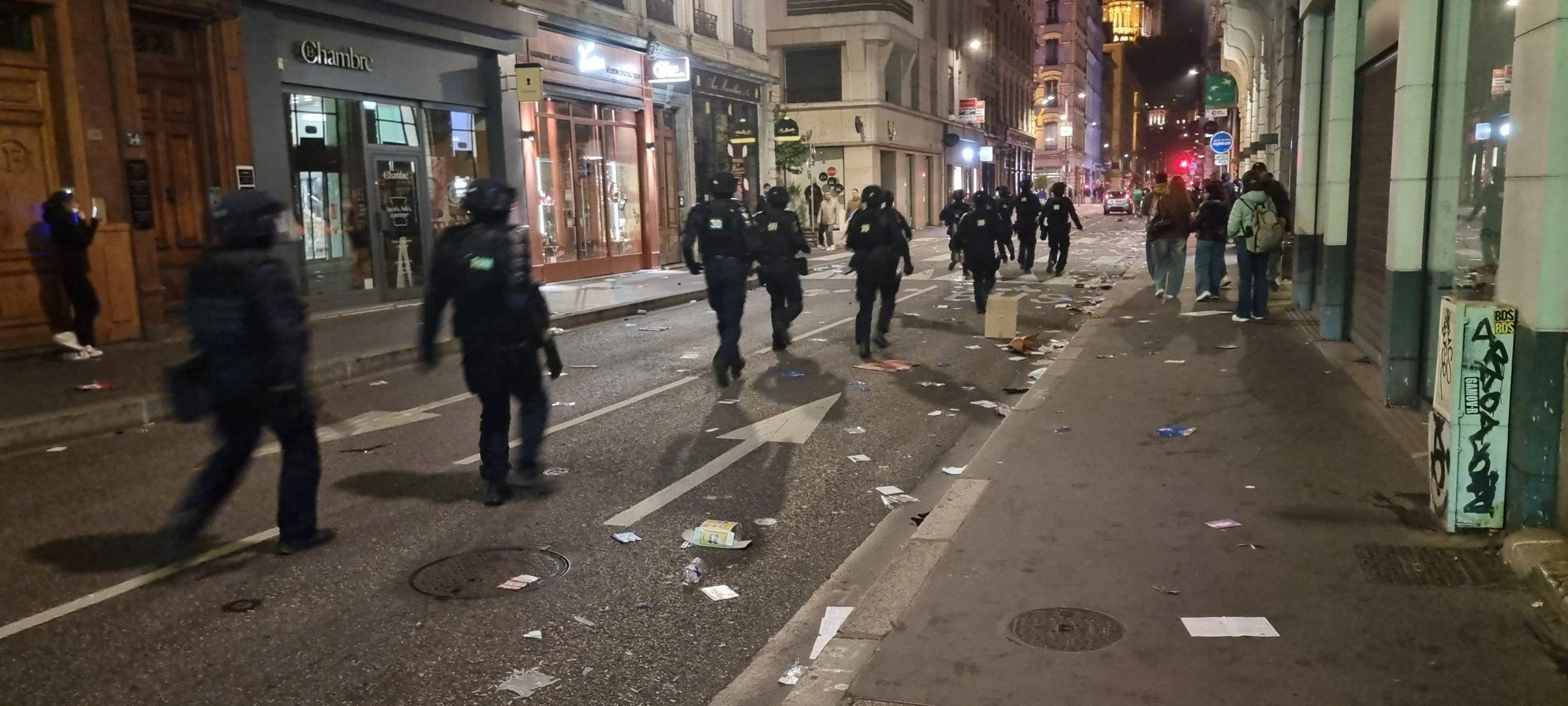 Une colonne de CRS remontant au pas de course une rue jonchée de débris, de nuit, rue Grenette à Lyon
