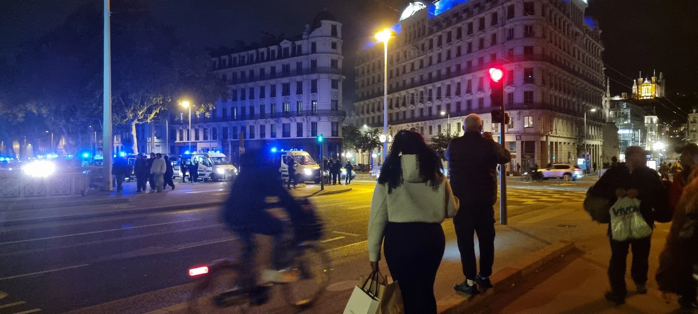 Fourgons de police aux gyrophares allumés et passants, de nuit, place des Cordeliers à Lyon