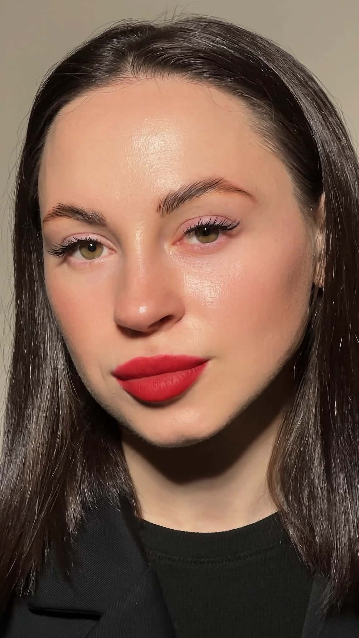 Close-up portrait of a woman with long brown hair, light makeup, red lipstick, and hazel eyes, wearing a black topSophisticated lash enhancements showcasing unmatched beauty expertise.