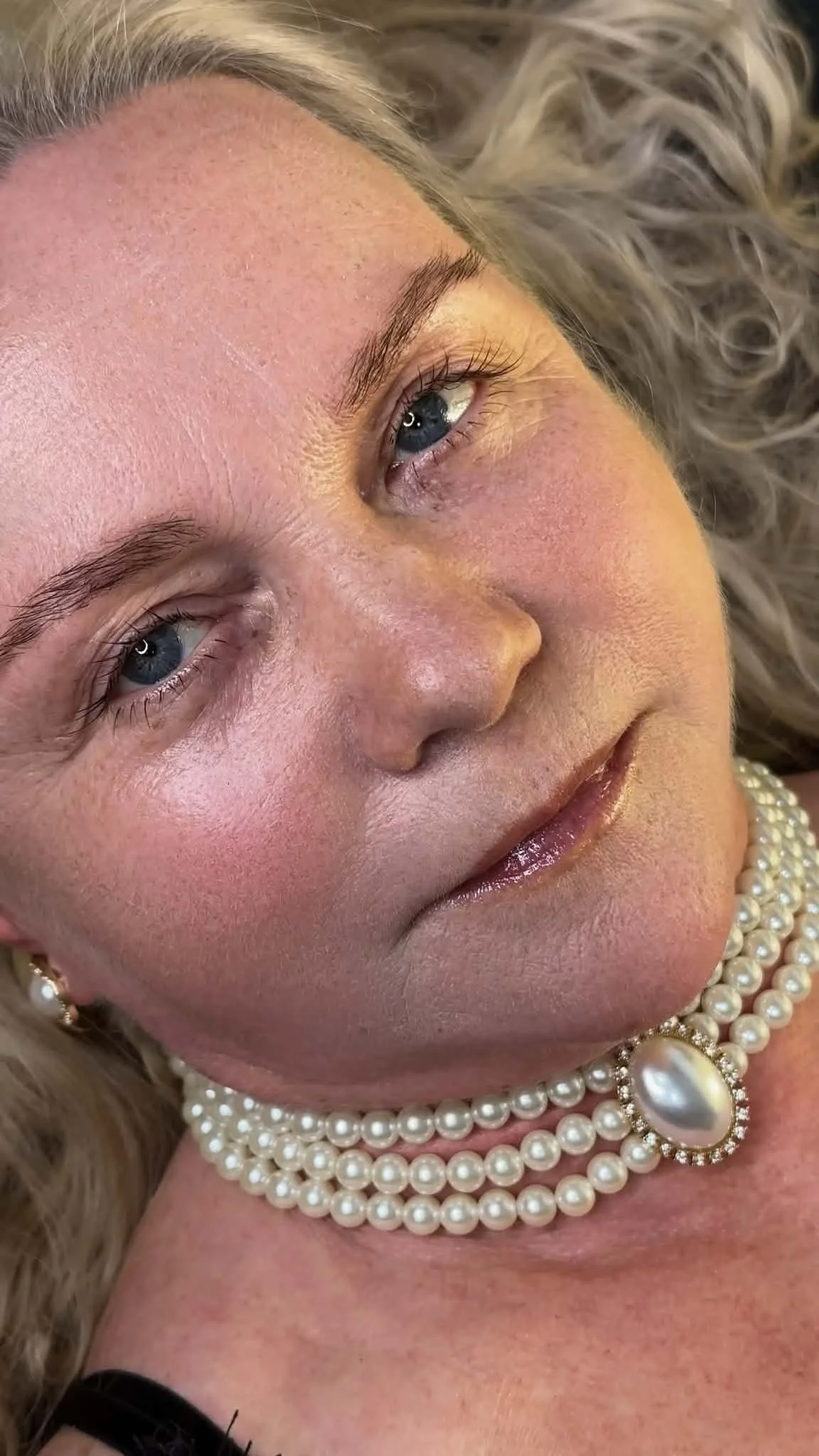 Close-up image of a woman’s face with blue eyes, wearing a pearl necklace and earrings.The pinnacle of lash design and beauty architecture.