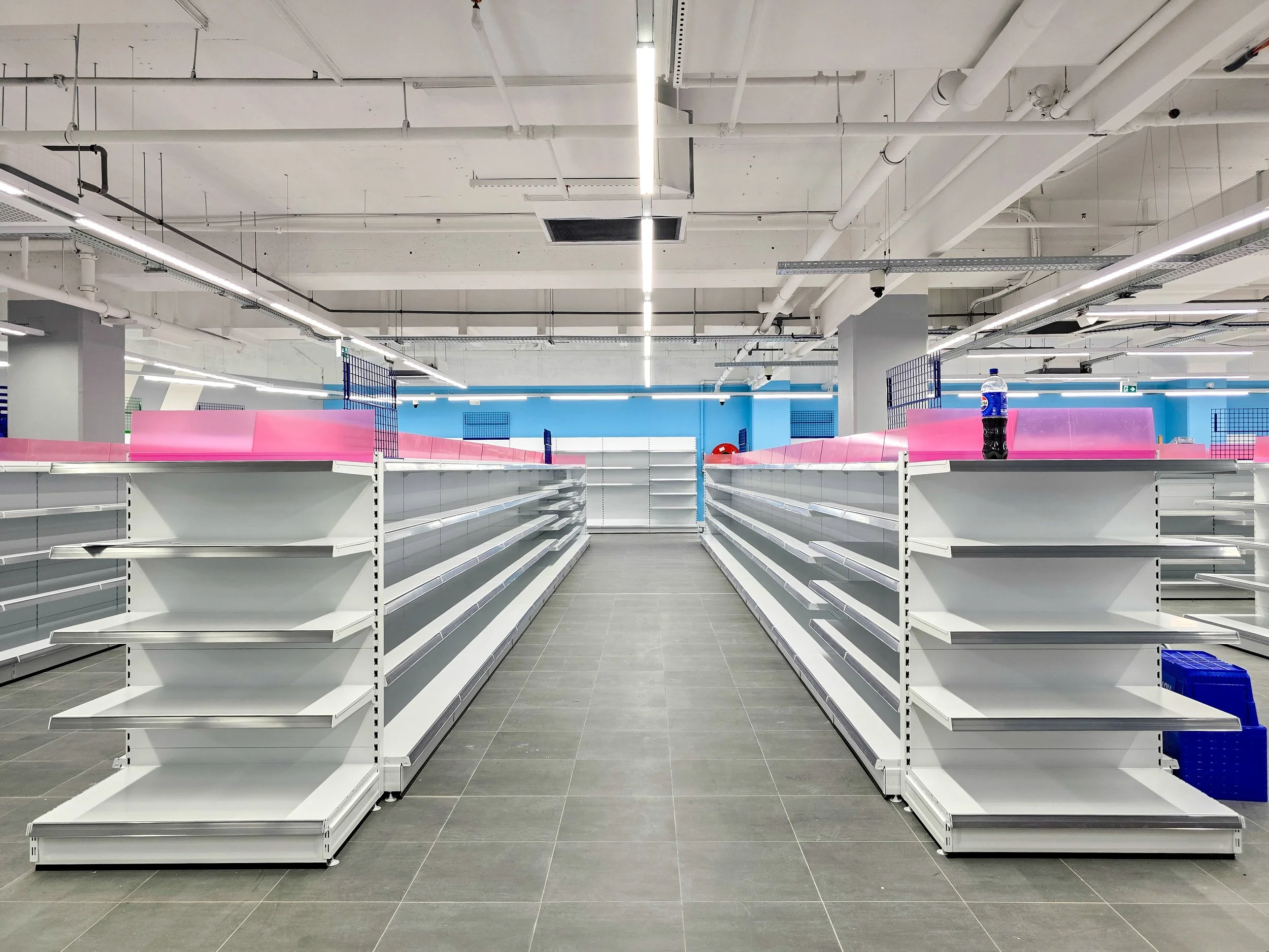 Rayons vides dans un magasin tout juste aménagé, avec quelques étagères métalliques blanches videset sol et plafond et peinture neufs.