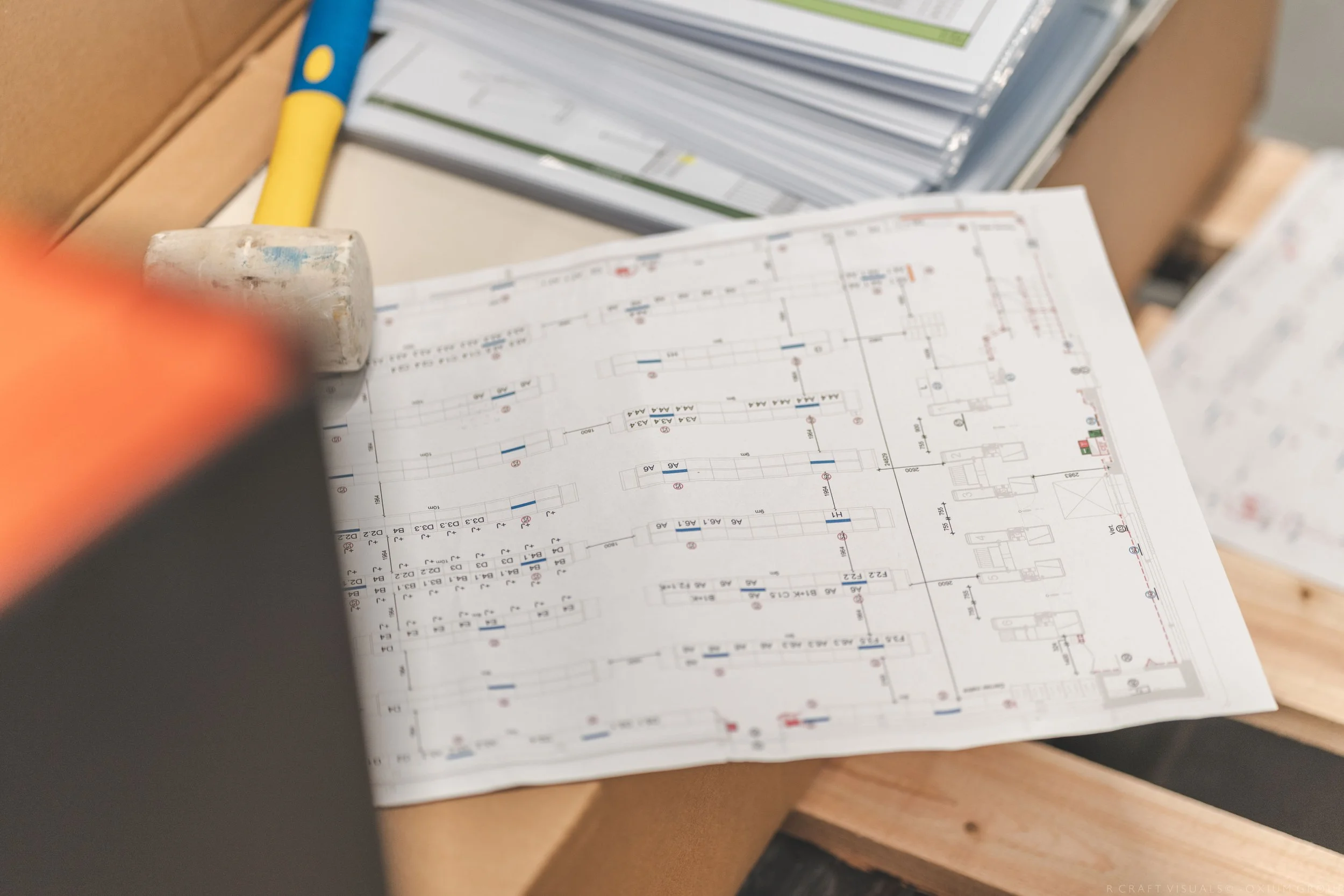 Plan architectural à plat sur une table en bois, avec des dessins techniques et des notes, entouré d'outils et de documents de travail.