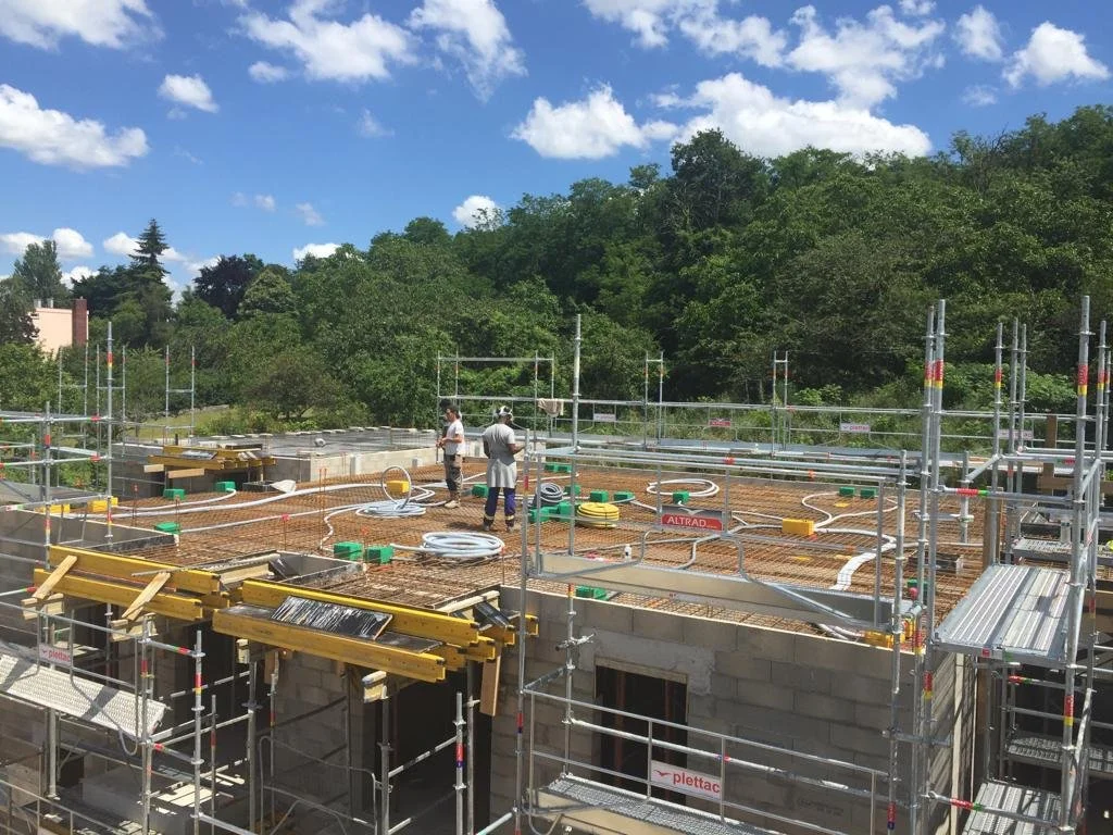 Construction d'un bâtiment avec des ouvriers, des échafaudages, des tuyaux, et un ciel bleu avec des nuages.