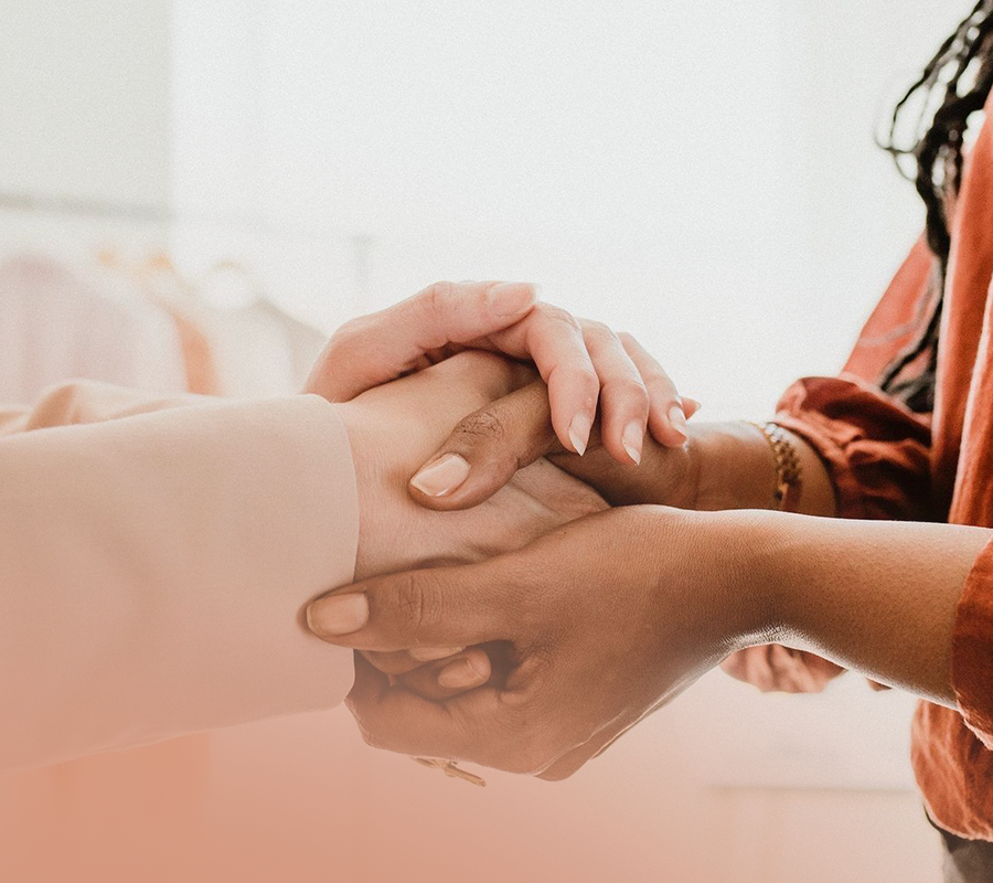 Close-up of two women holding hands, one with darker skin and the other with lighter skin, in a gentle, caring manner.