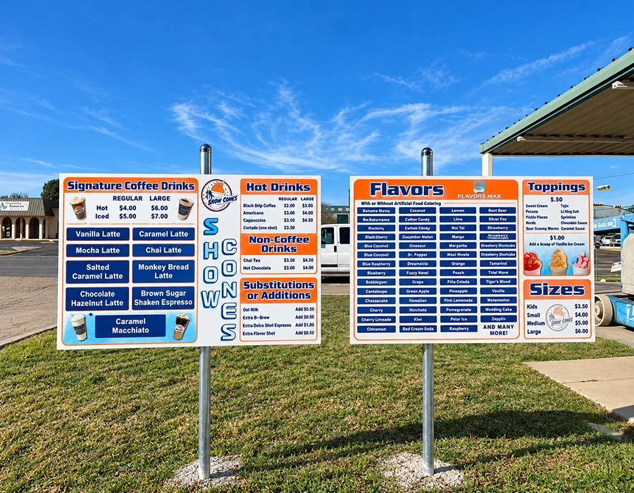 Large menu boards for a coffee stand listing various hot, iced, and non-coffee drinks, flavors, toppings, sizes, and prices.