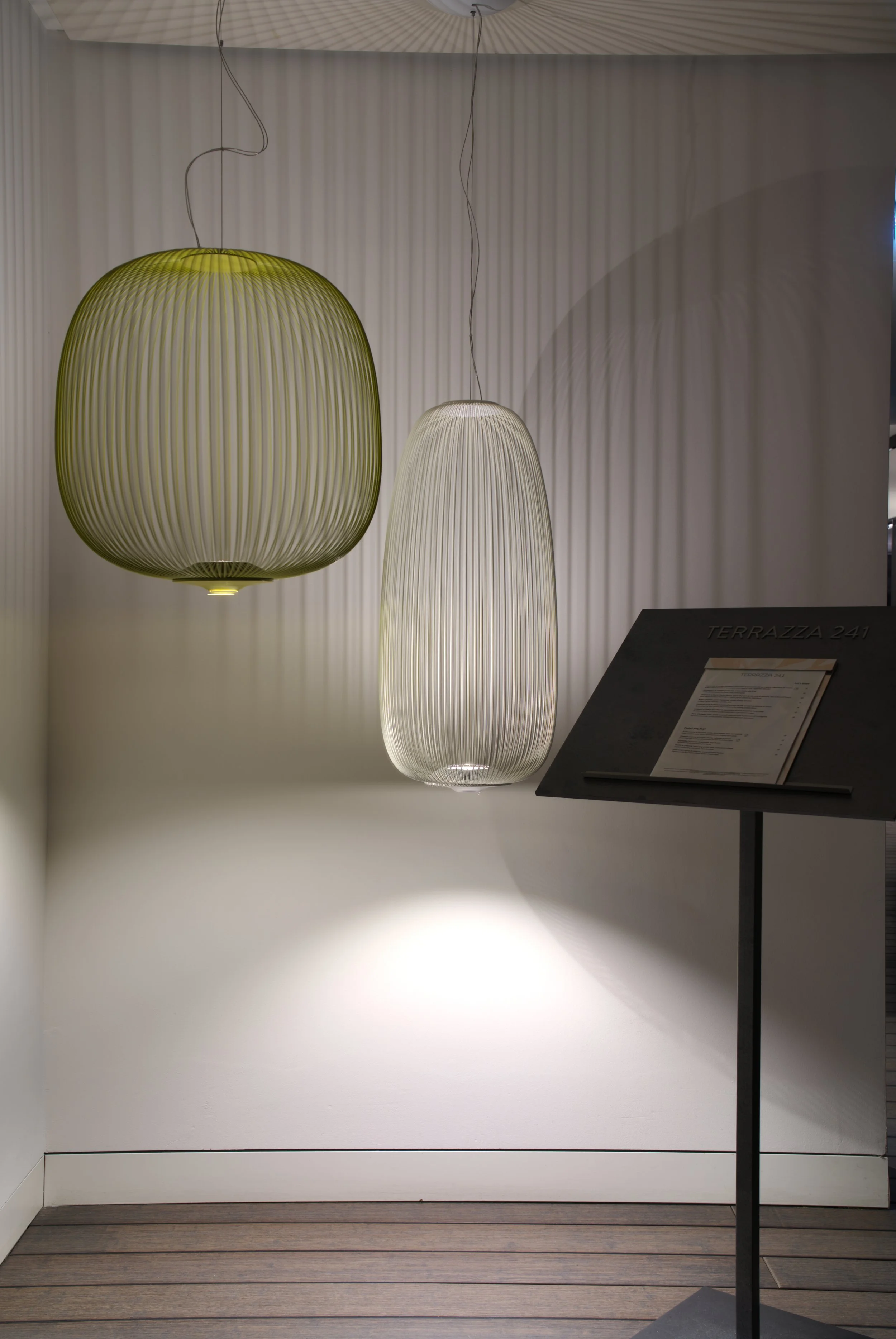 Two modern hanging lamps, one yellow and one white, hanging in a minimalist interior with a textured wall and a sign labeled 'Terrazza 241'.