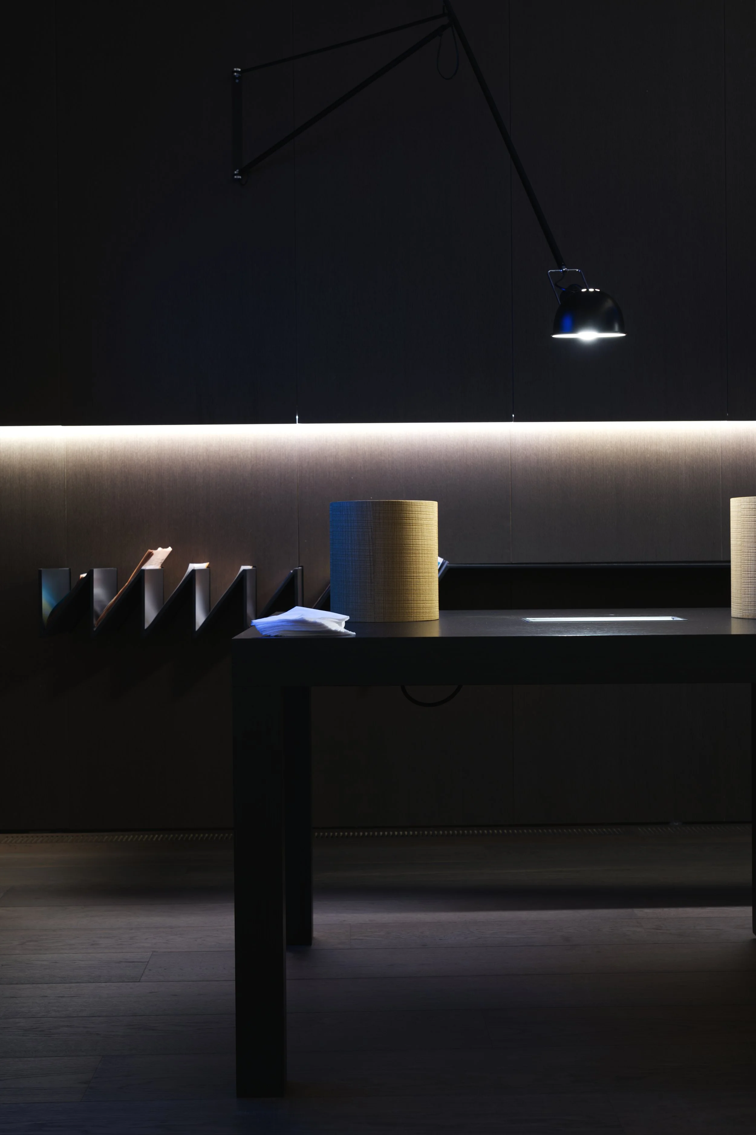Modern reception desk area with a black wall, wall-mounted black lamp, and file organizers on the desks.