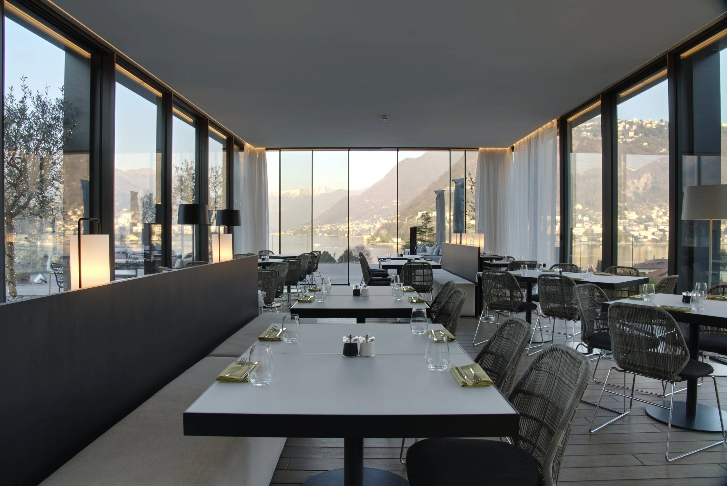 Modern restaurant with large glass windows and mountain views, set for dining with tables, chairs, and neatly folded napkins.